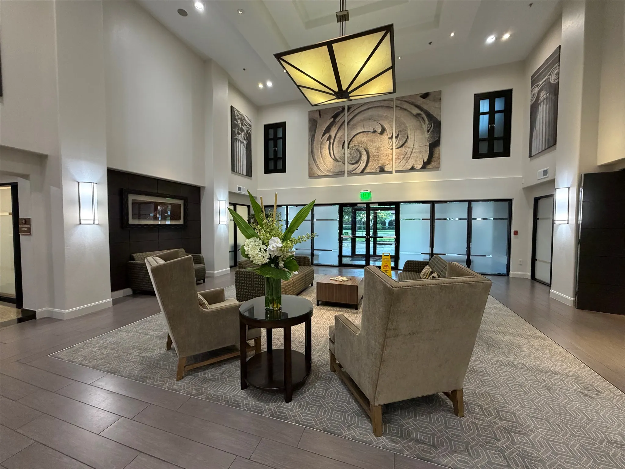 Double-height ceiling, large decorative light fixture, wall-mounted sconces, transom windows, and wood-finish flooring