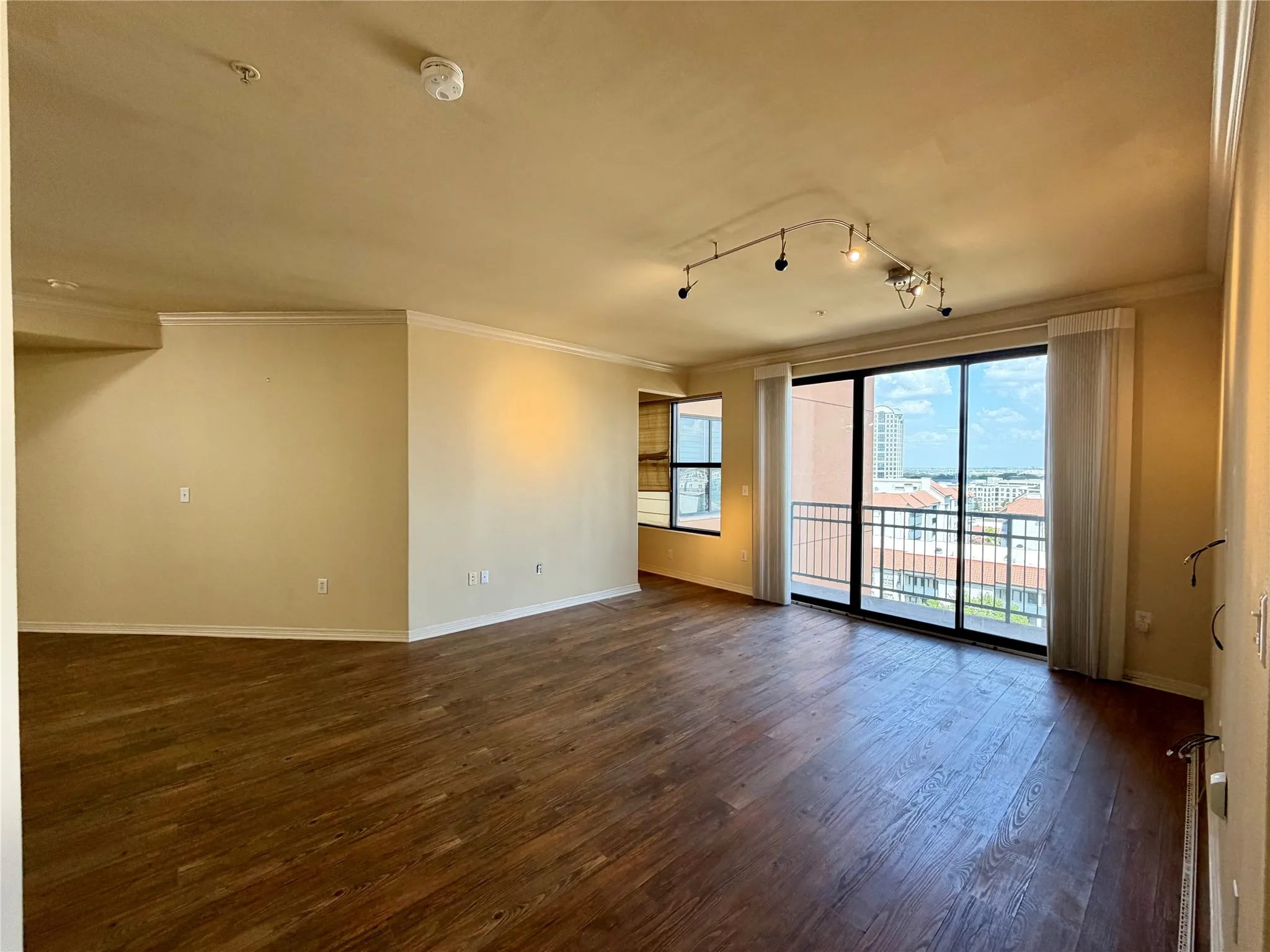 Expansive living area featuring wood-finish flooring, track lighting, crown molding, and large sliding glass doors opening to an exterior balcony