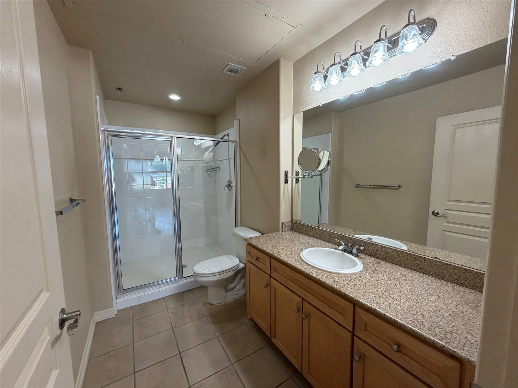 Tiled flooring, wood-finish vanity with ample storage, integrated sink, large vanity mirror, and shower enclosure with sliding glass door