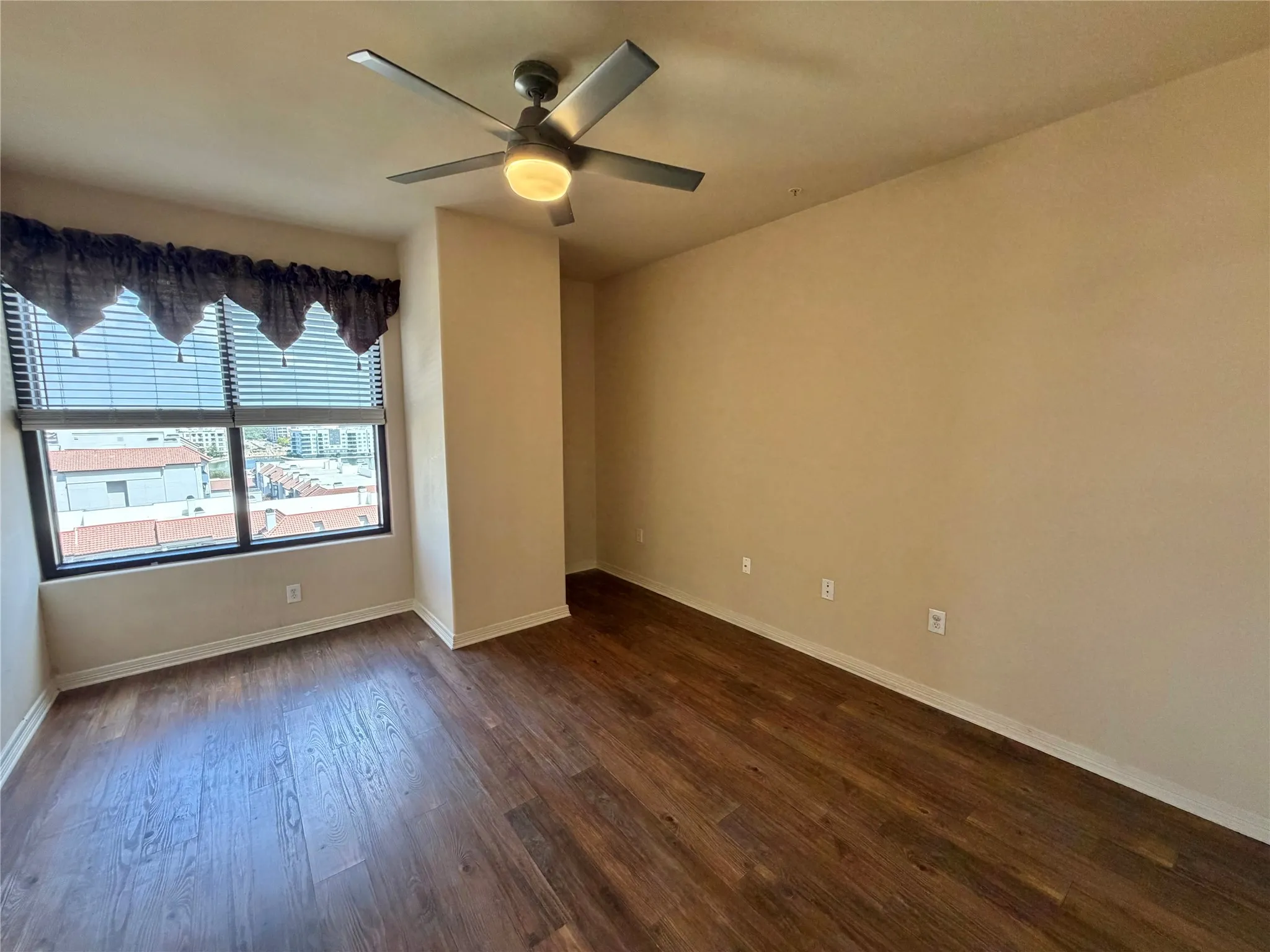 Room featuring wood-finish flooring, a ceiling fan with integrated lighting, and a large window with blinds