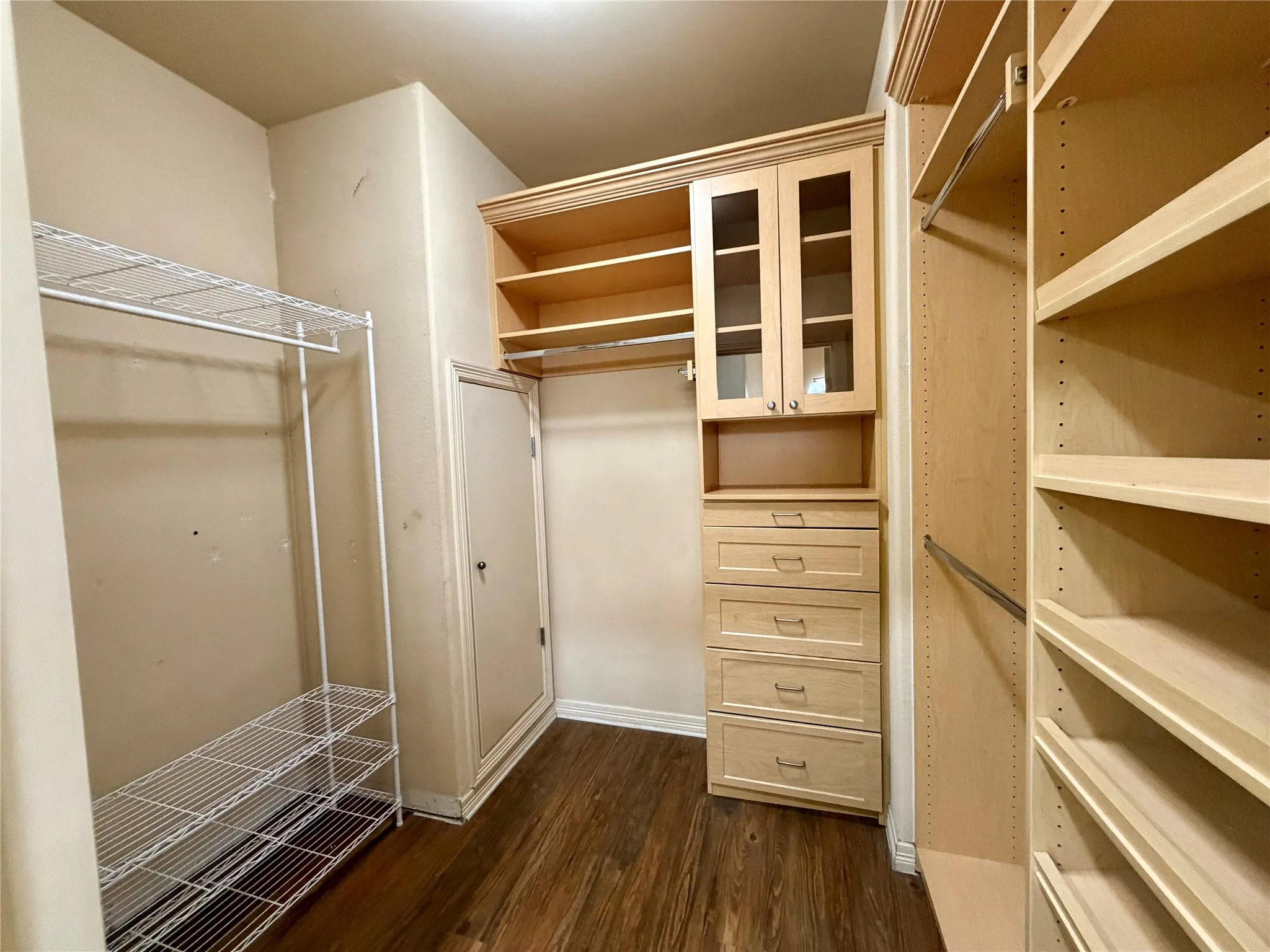 Closet featuring wood-finish flooring, built-in cabinetry with glass-front doors, multiple drawers, and adjustable shelving units