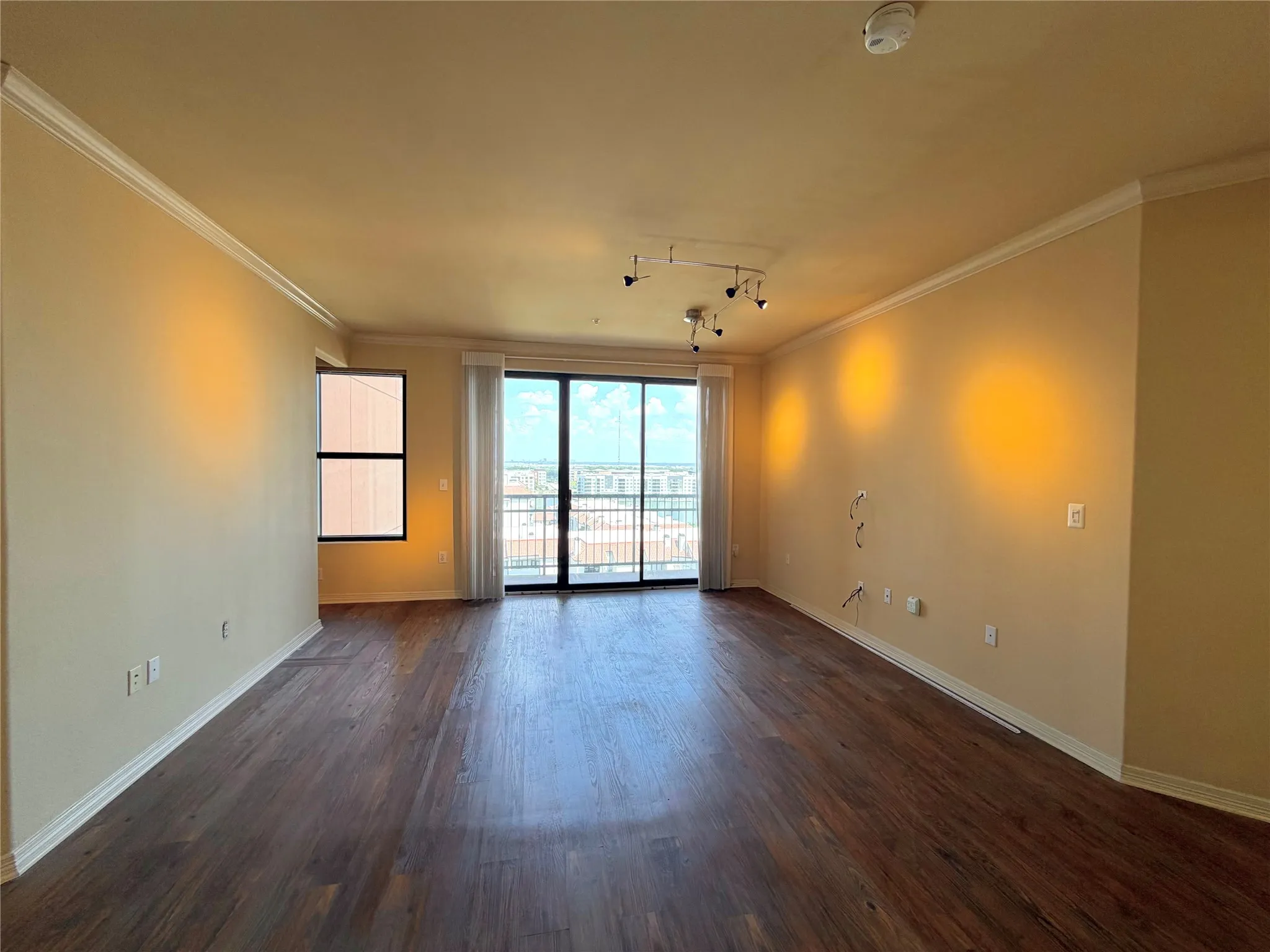 Wood-finish flooring, crown molding, track lighting, and sliding glass doors with balcony access