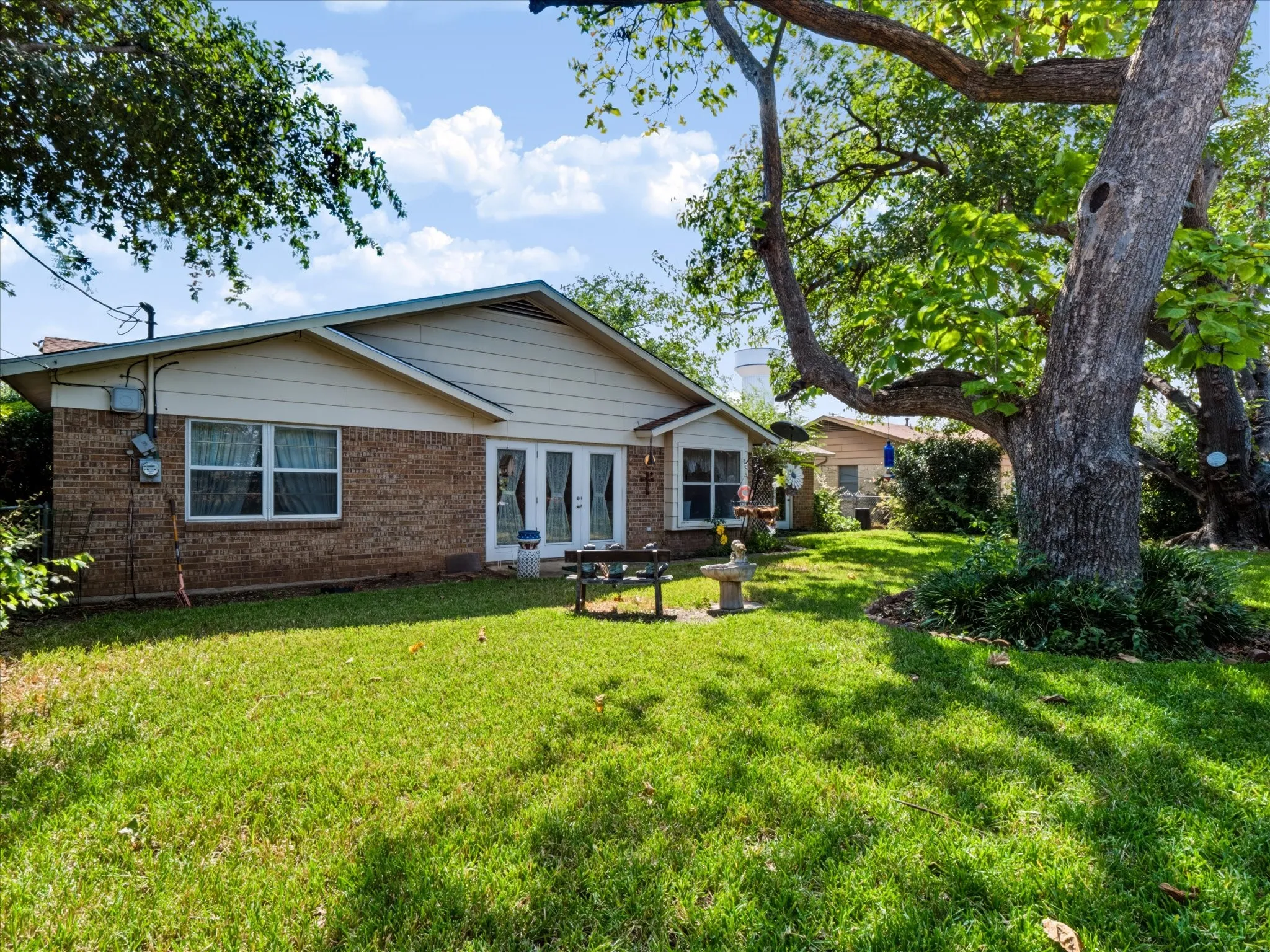 Brick exterior with a gabled roofline, multiple windows, and a set of white French doors opening to a lush green lawn