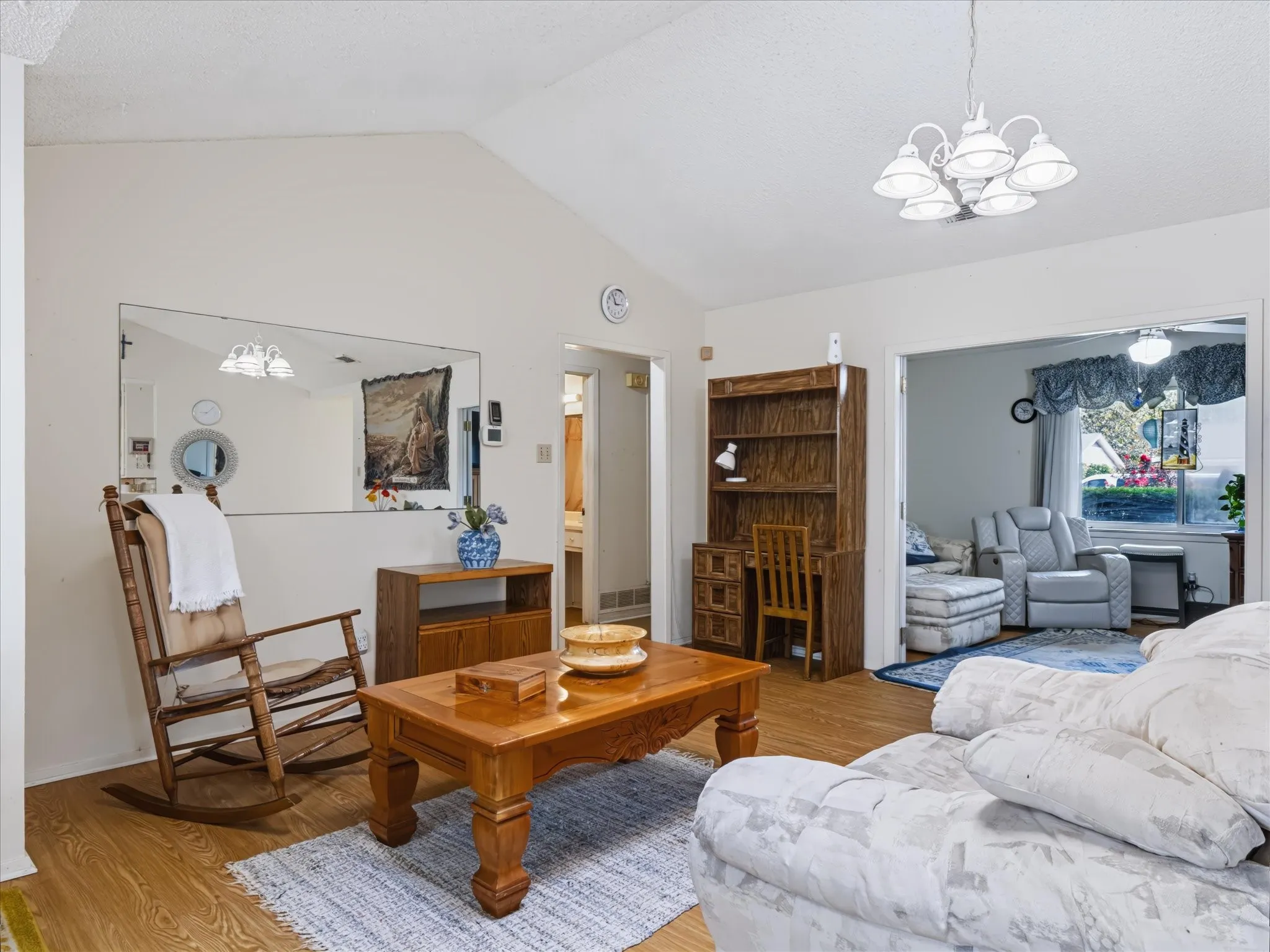 Vaulted ceiling, wood-finish flooring, built-in desk with shelving, overhead chandelier lighting, and a wall-mounted mirror