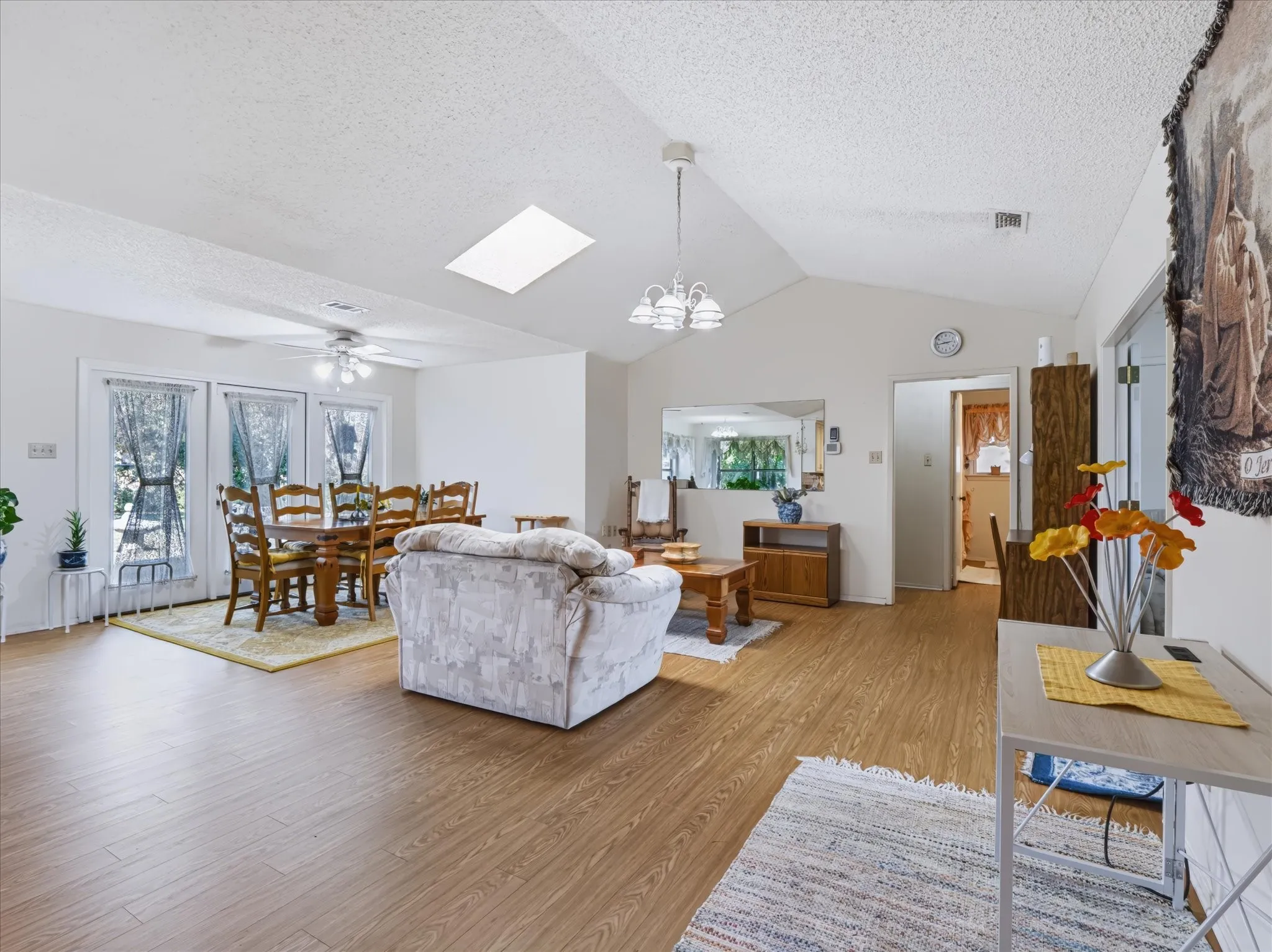 Vaulted ceiling with skylight, wood-finish flooring, and a ceiling fan