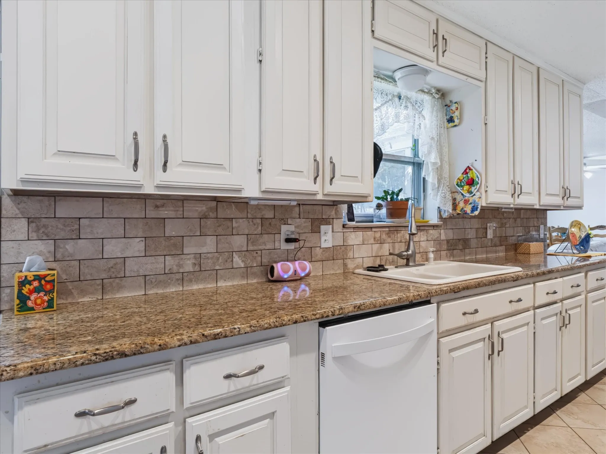 White cabinetry, subway tile backsplash, granite-style countertops, stainless steel sink with gooseneck faucet, and an integrated dishwasher