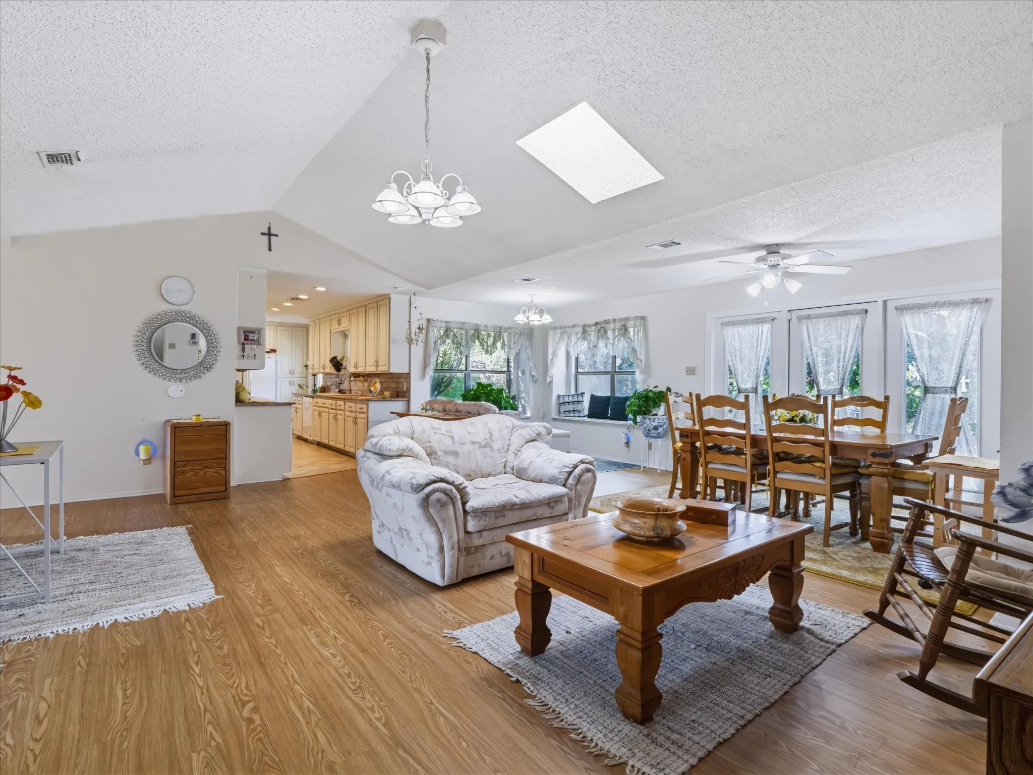 Vaulted ceiling with an overhead light fixture, wood-finish flooring, and a kitchen with wood cabinetry