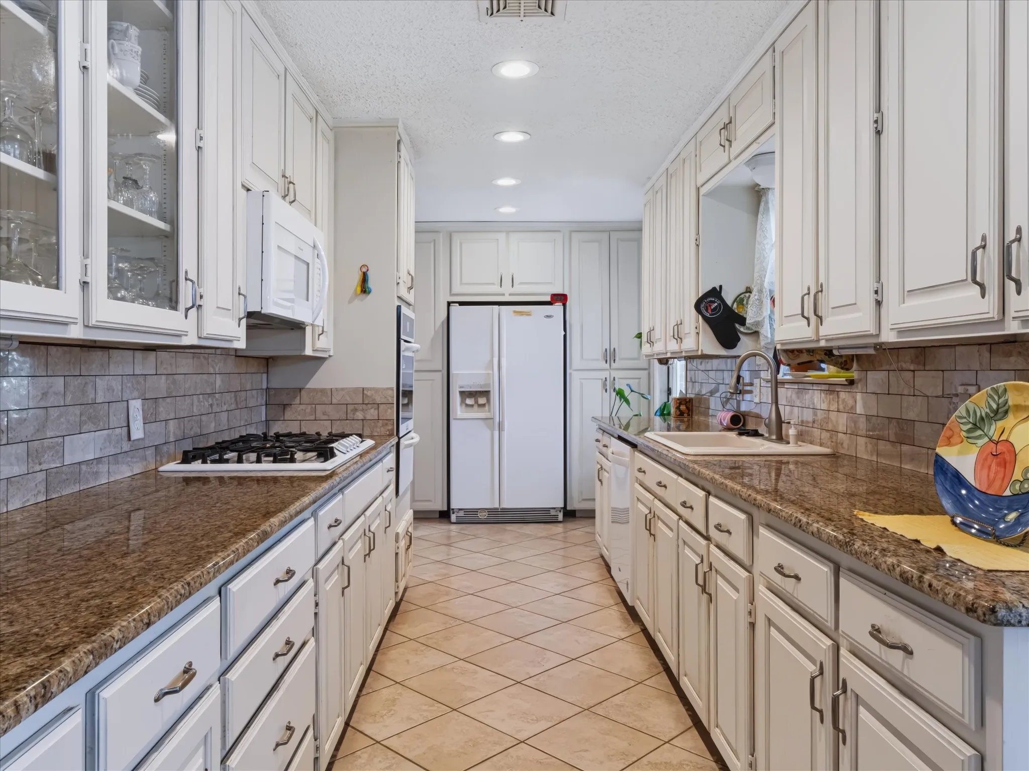 Galley kitchen featuring white cabinetry, stone-finish countertops, subway tile backsplash, and recessed lighting