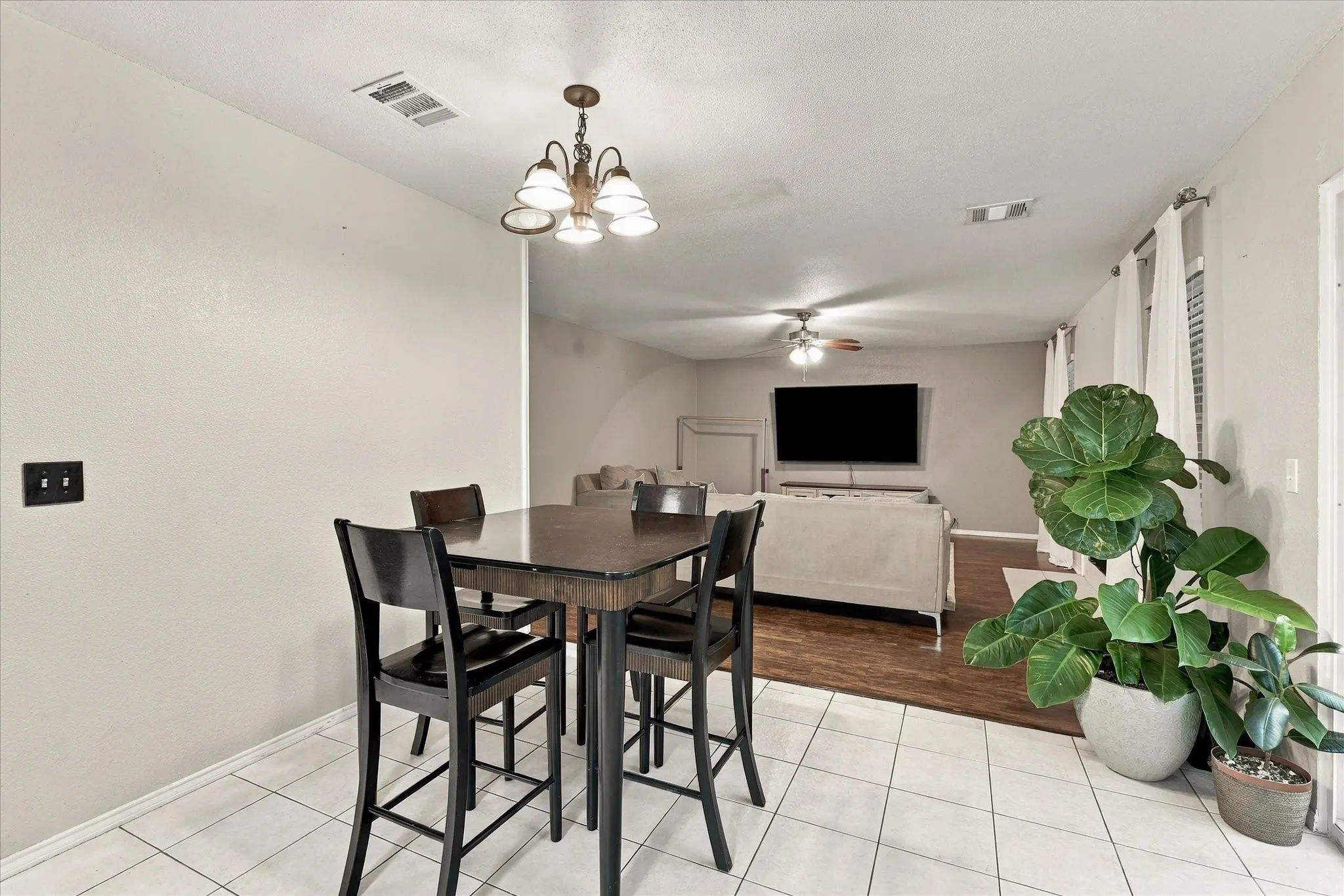 Tiled flooring in the foreground, wood-finish flooring in the background, ceiling-mounted light fixture, recessed lighting, and a ceiling fan