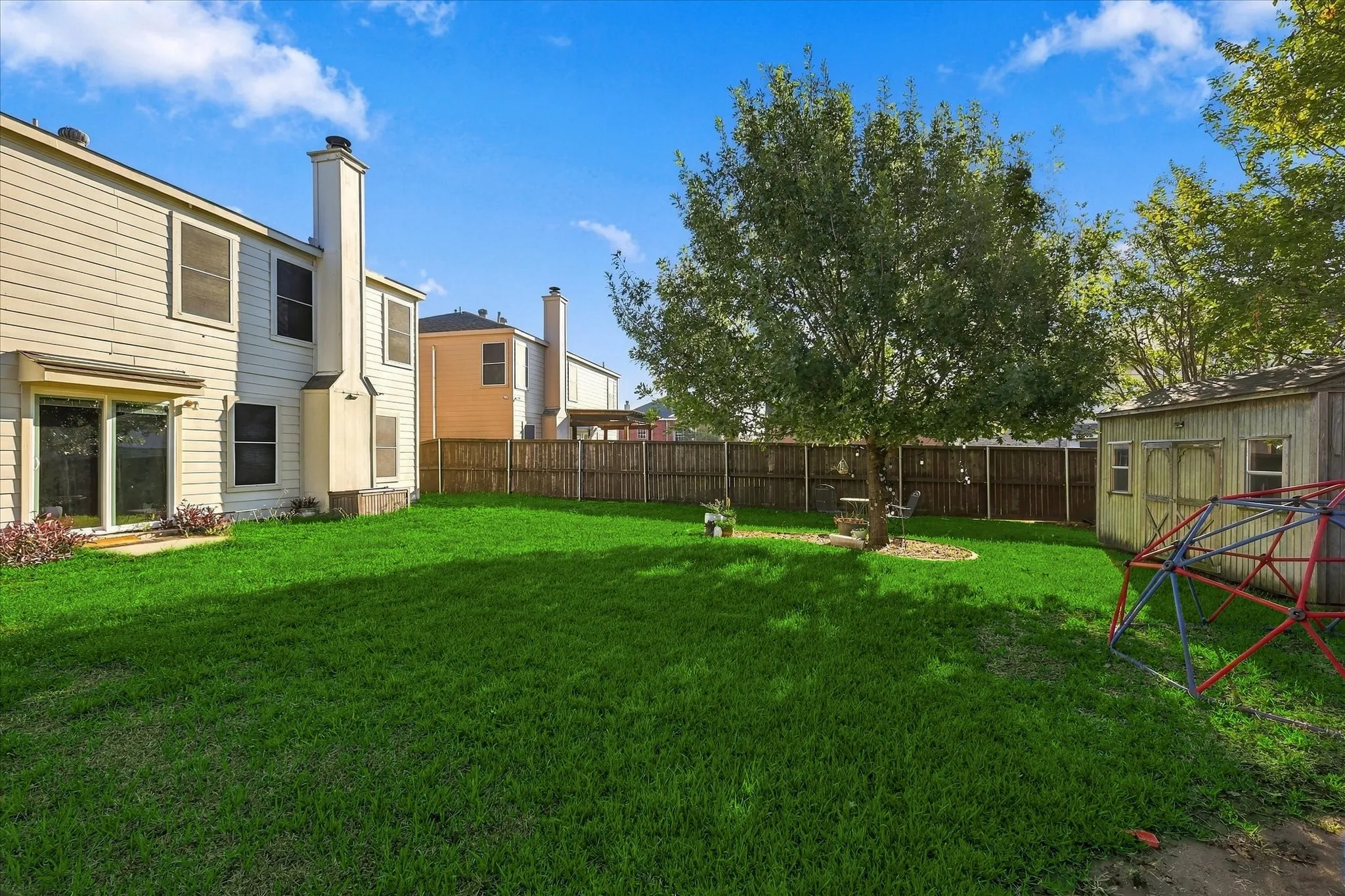 Expansive backyard with a manicured lawn, established tree, and wood privacy fencing