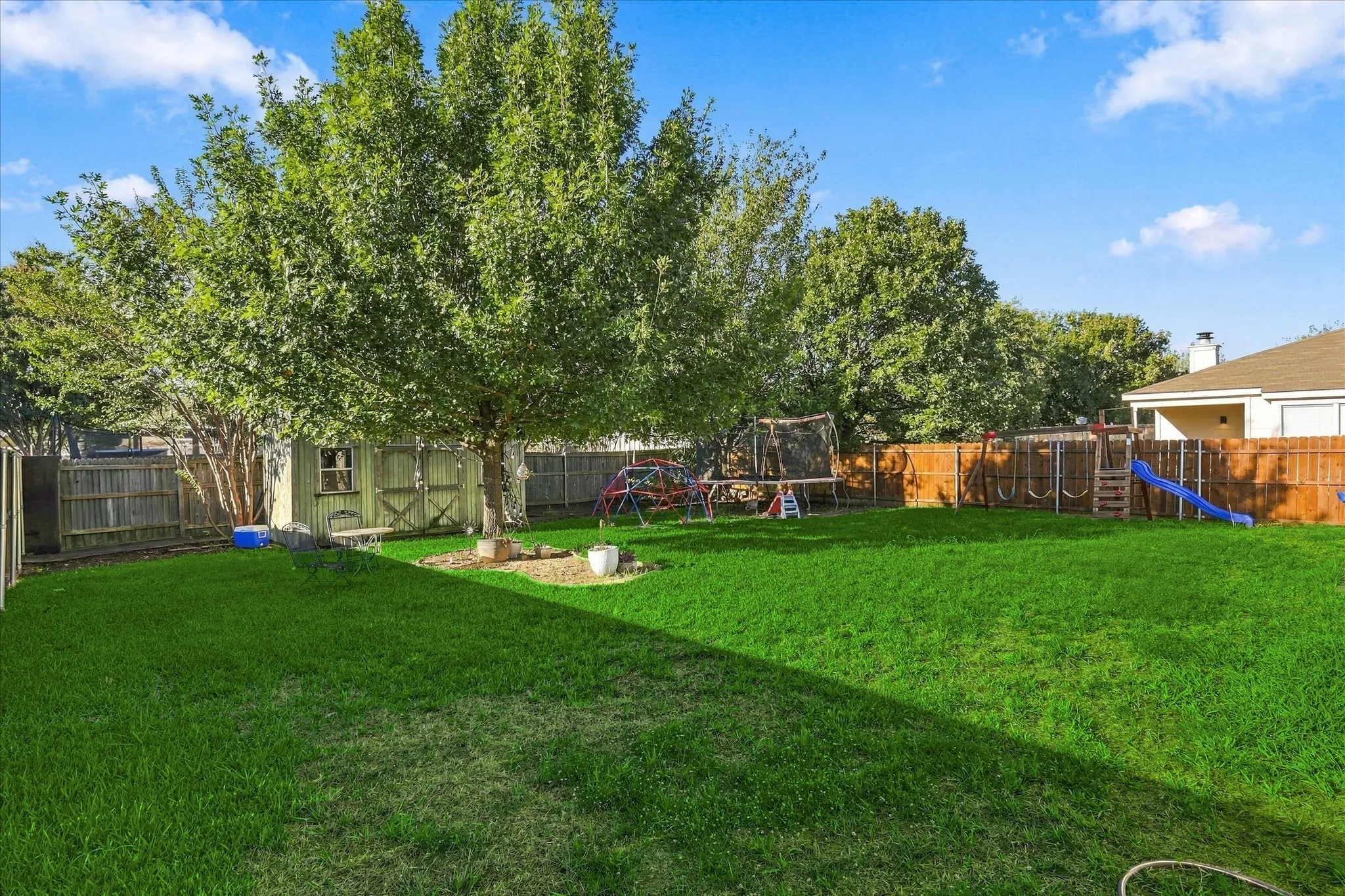 Expansive backyard featuring a manicured lawn, wood fencing, and mature trees
