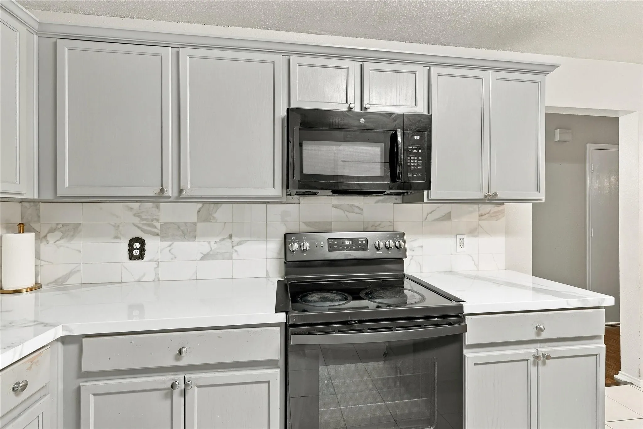 White countertops, gray shaker-style cabinetry, black over-the-range microwave, and a black electric range