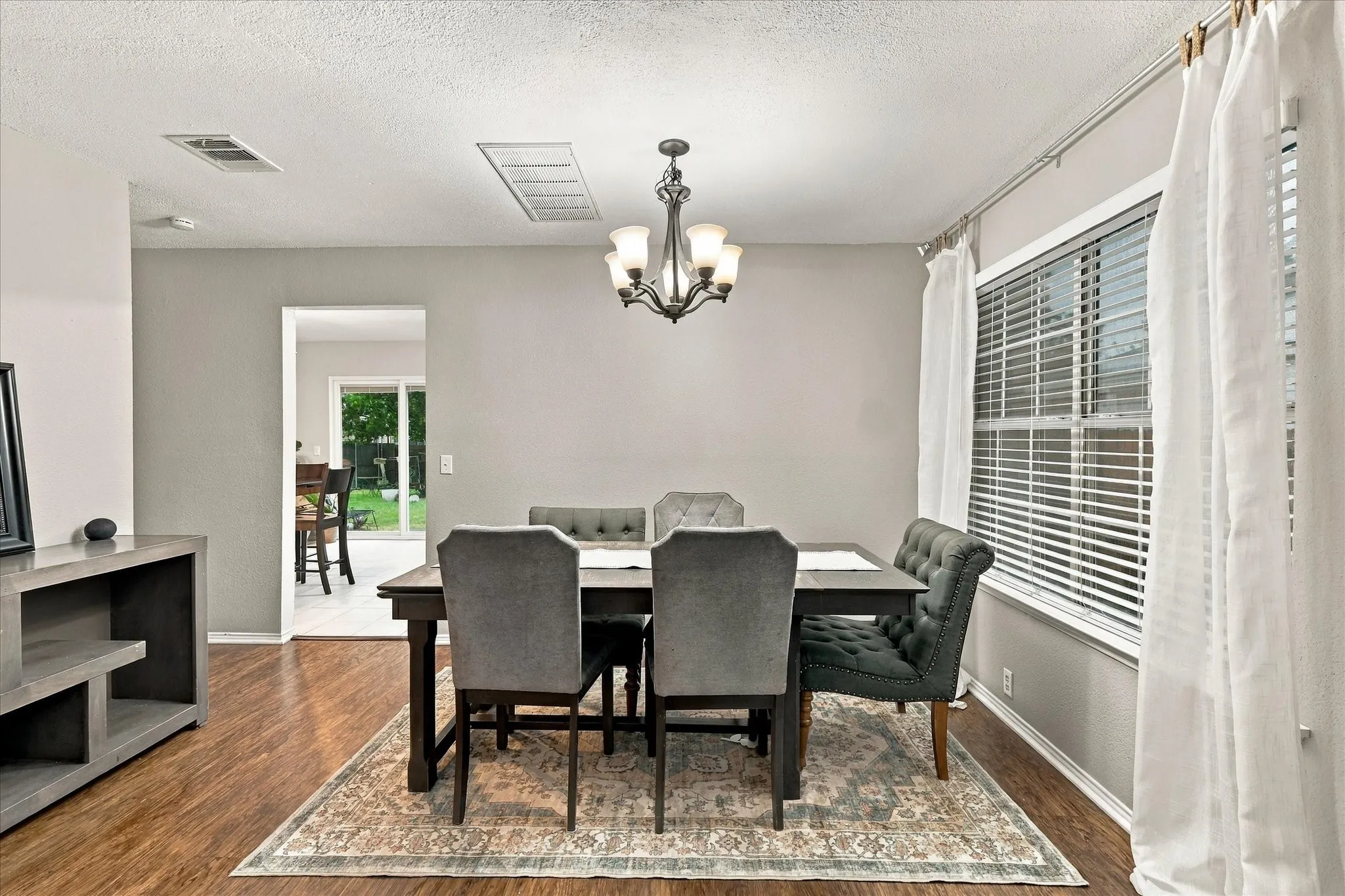 Wood-finish flooring with a large window featuring blinds, a chandelier with frosted glass shades, and a framed doorway