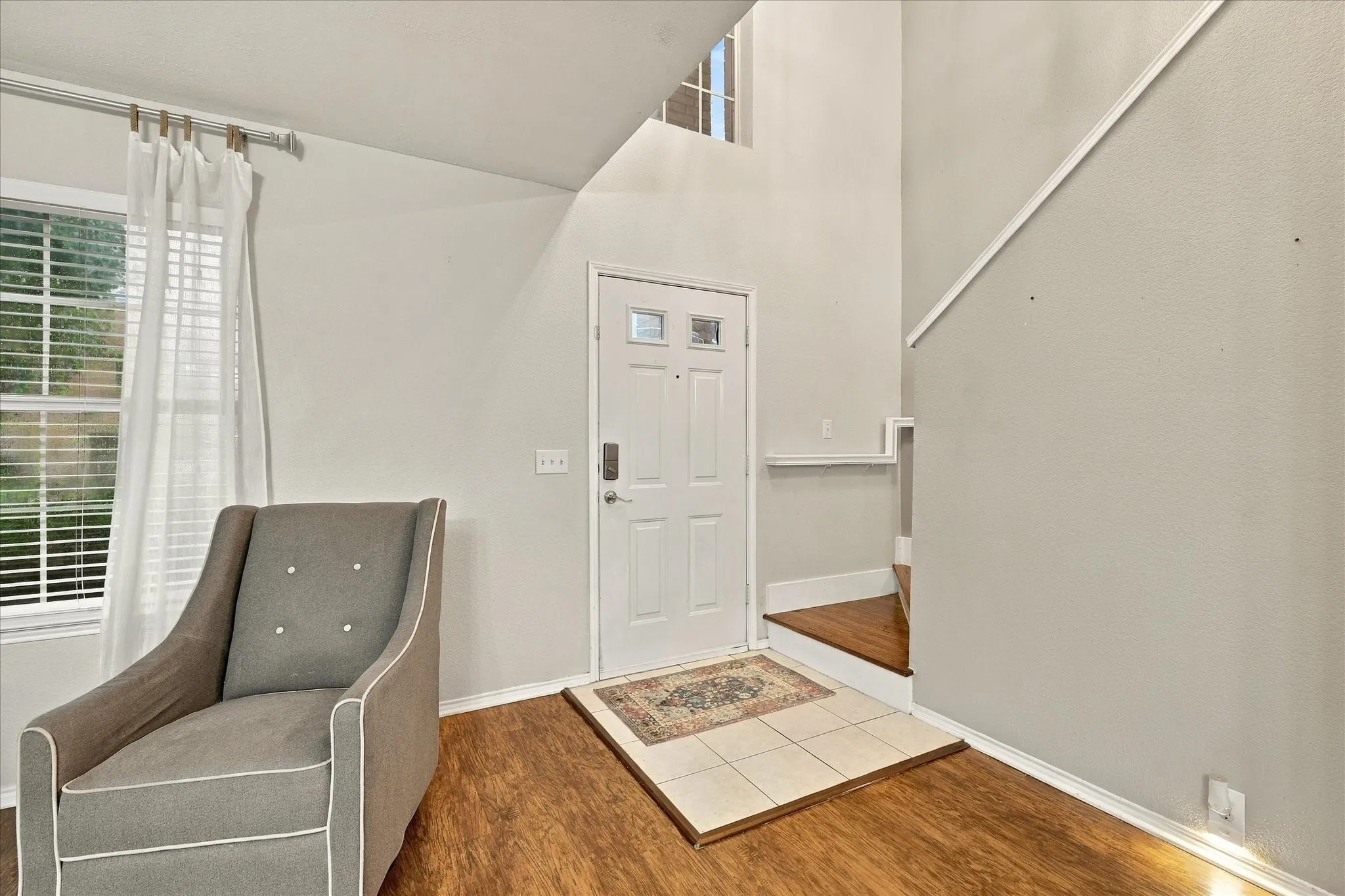 Wood-finish flooring, white window blinds, white door with glass insert, tiled entry, and wood stairs with white risers