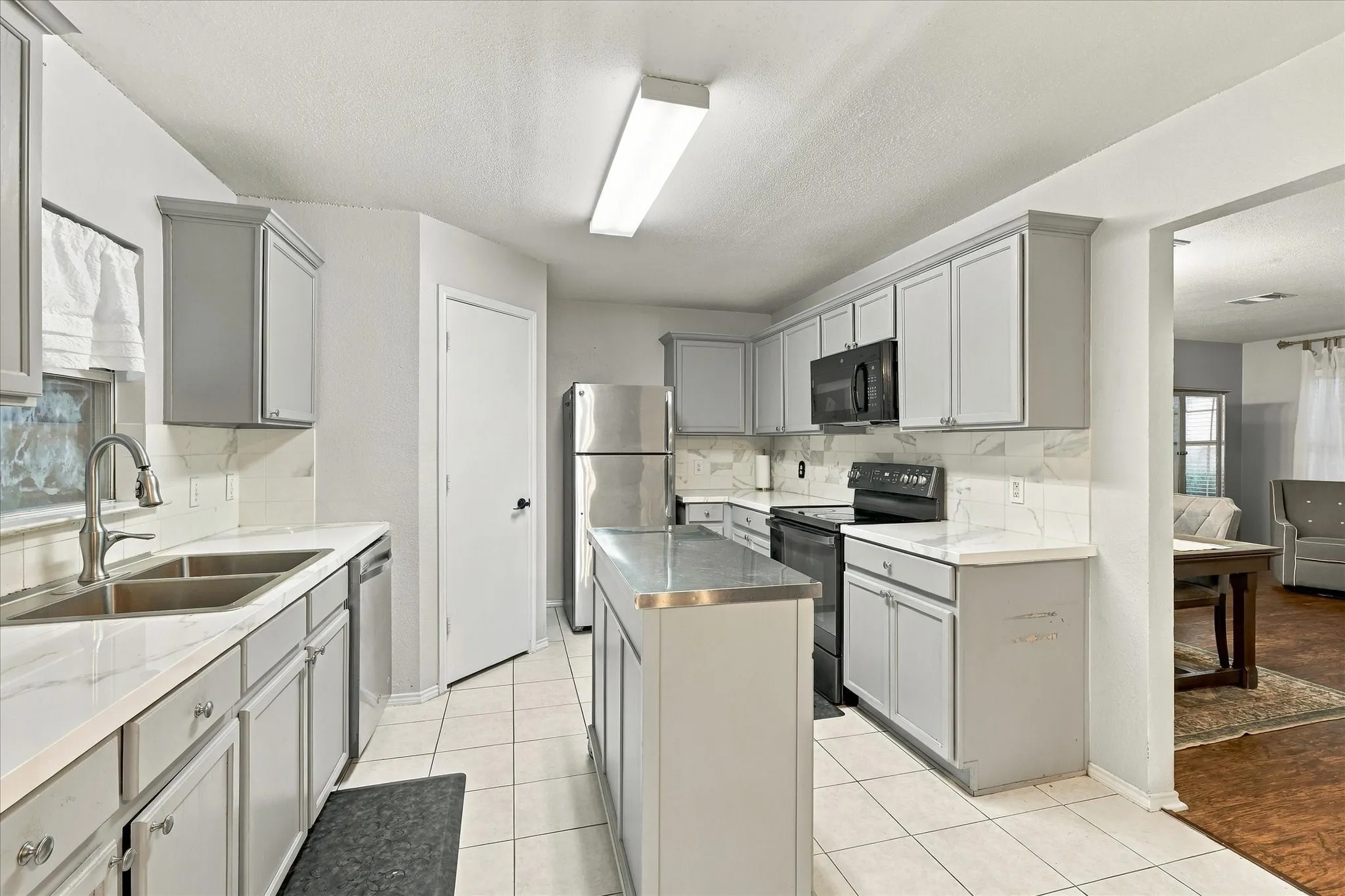 Kitchen featuring light gray cabinetry, stainless steel appliances, white countertops, a matching tile backsplash, and an island with a stainless steel surface