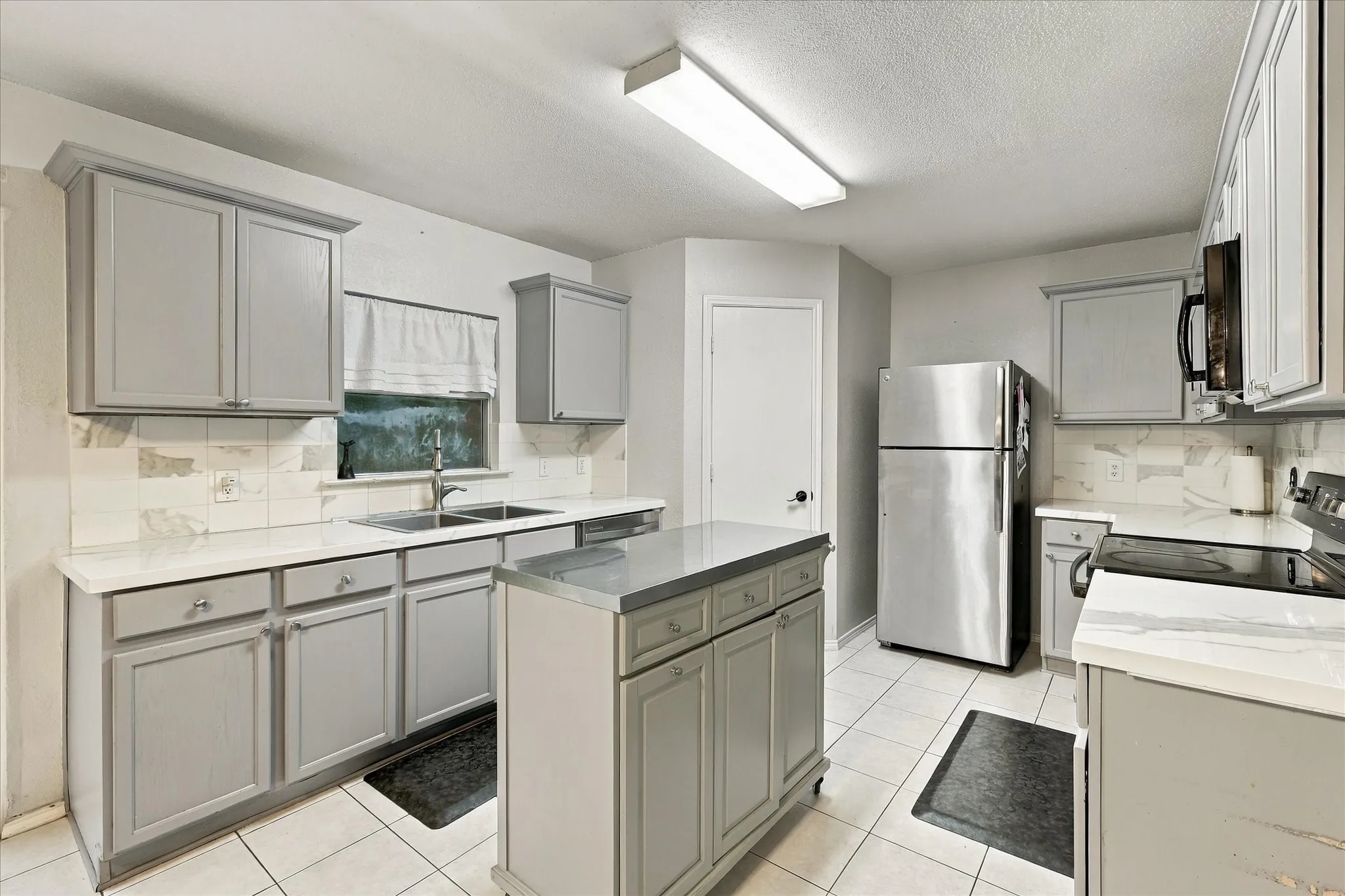 Kitchen featuring light gray cabinetry, white countertops, tile flooring, stainless steel appliances, and a central island with a contrasting countertop