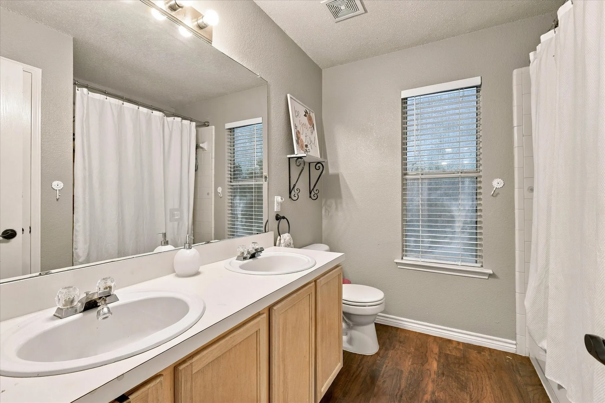 Dual vanity with white oval sinks, wood-finish cabinetry, and a large wall-mounted mirror