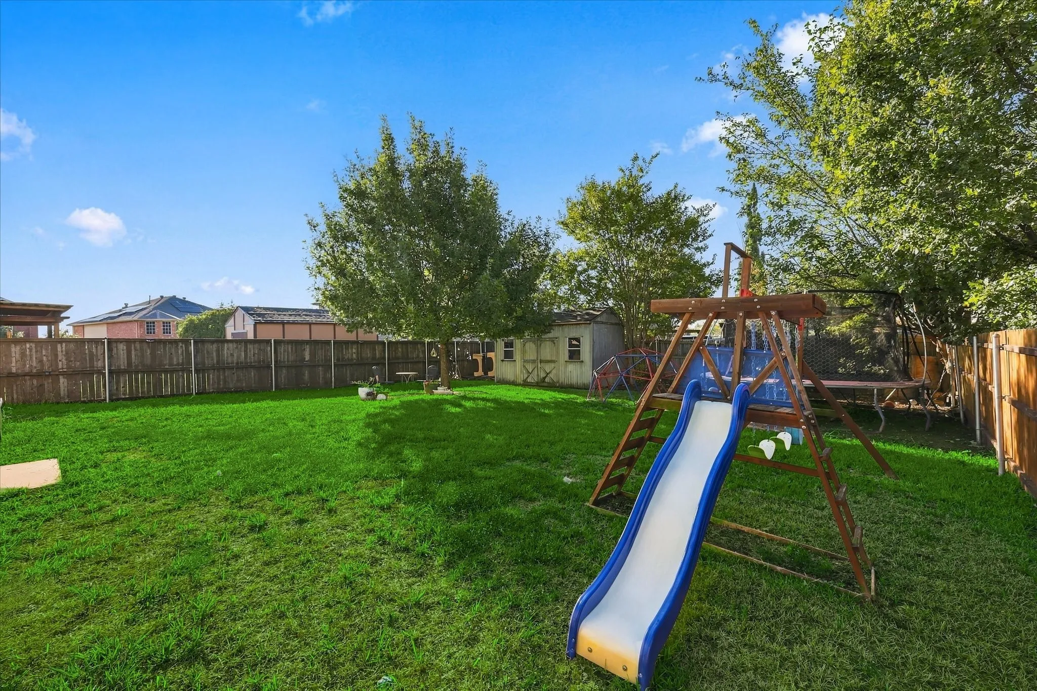 Expansive backyard featuring a manicured lawn, wood privacy fencing, a storage shed, and mature trees