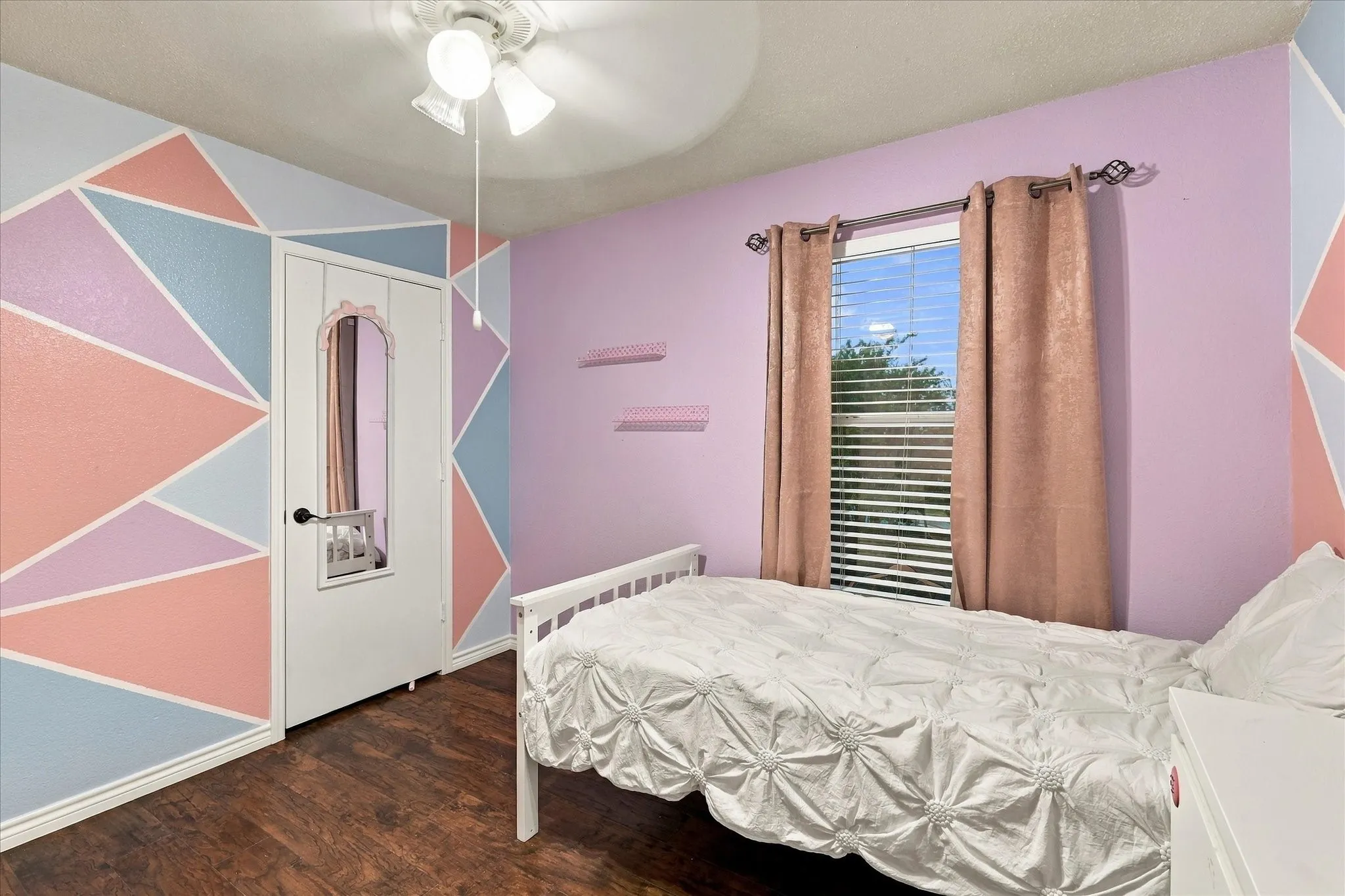 Wood-finish flooring, ceiling fan, window with blinds, and geometric accent wall