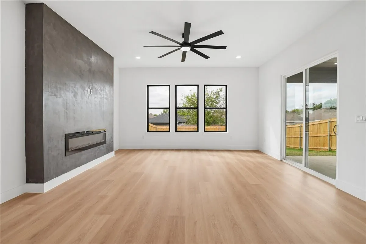 Wood-finish flooring, accent wall with built-in linear fireplace, three black-framed windows, and sliding glass door