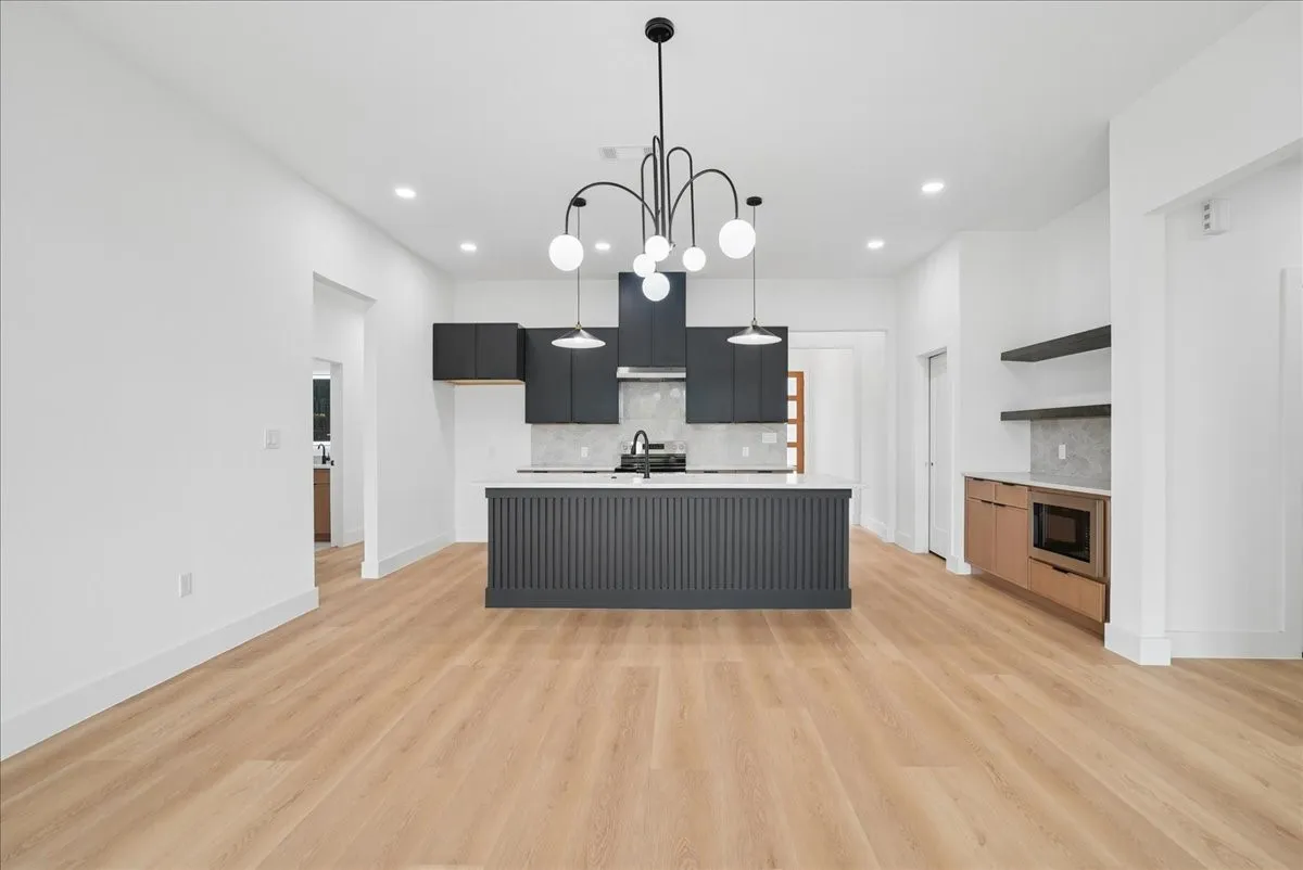 Wood-finish flooring throughout, kitchen island with fluted paneling, matte black cabinetry, built-in microwave, and open shelving