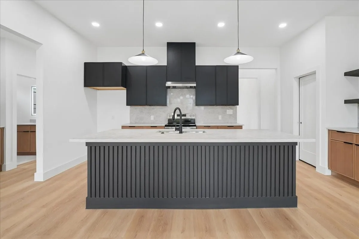 Modern kitchen with a slatted island, light wood-finish flooring, recessed lighting, and dual pendant lights