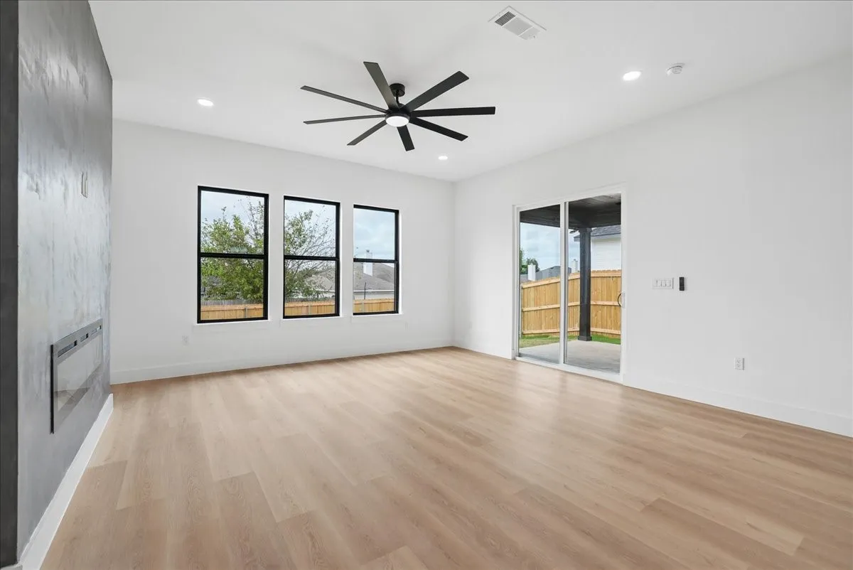 Spacious room featuring light wood-finish flooring, a contemporary ceiling fan, recessed lighting, a built-in linear fireplace, and an expansive sliding glass door to the exterior