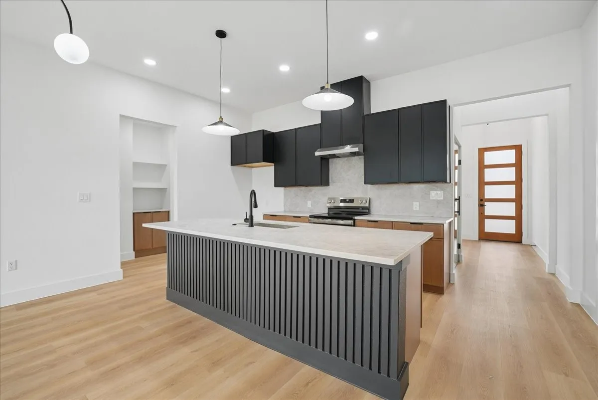 Kitchen featuring a large island with a light-toned countertop, black cabinetry, stainless steel appliances, and wood-finish flooring