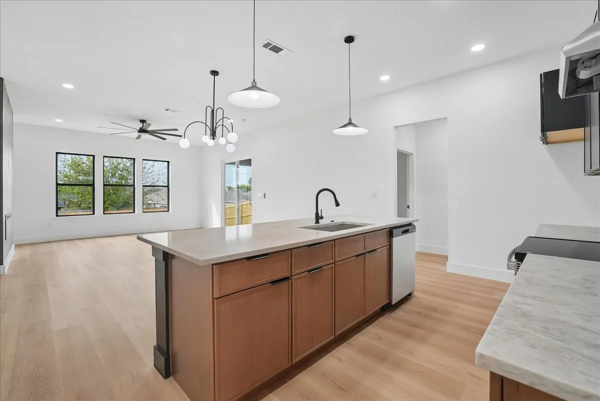 Kitchen island with integrated sink, stainless steel dishwasher, and pendant lighting