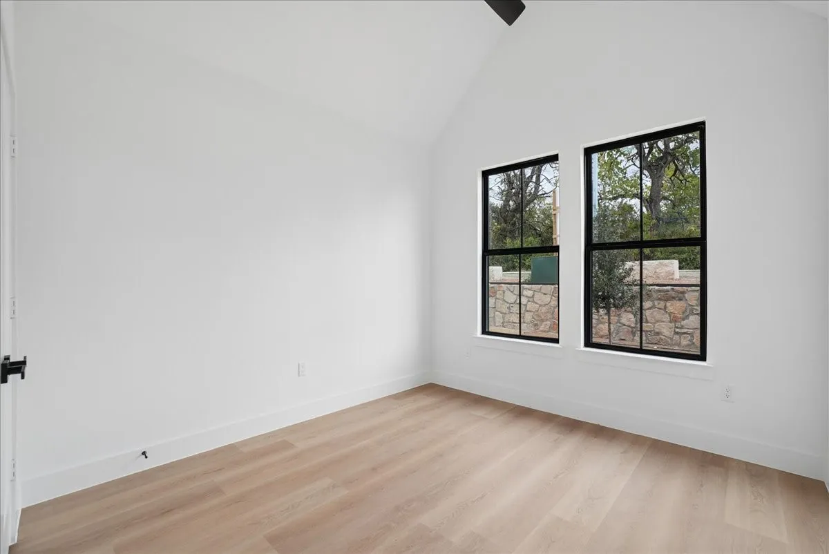Vaulted ceiling, recessed lighting, wood-finish flooring, black-framed windows, and a stone retaining wall