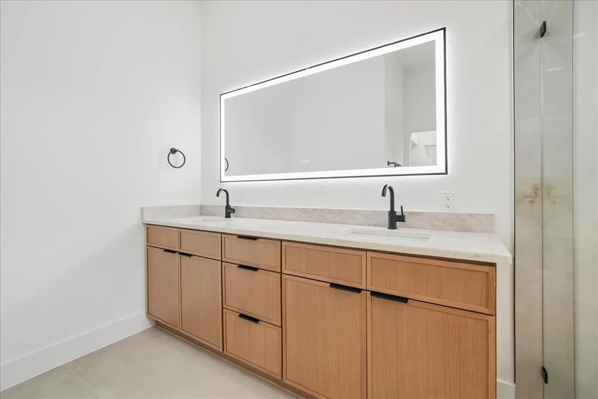 Dual vanity with wood-finish cabinetry, light-toned countertop, integrated sinks, and matte black fixtures
