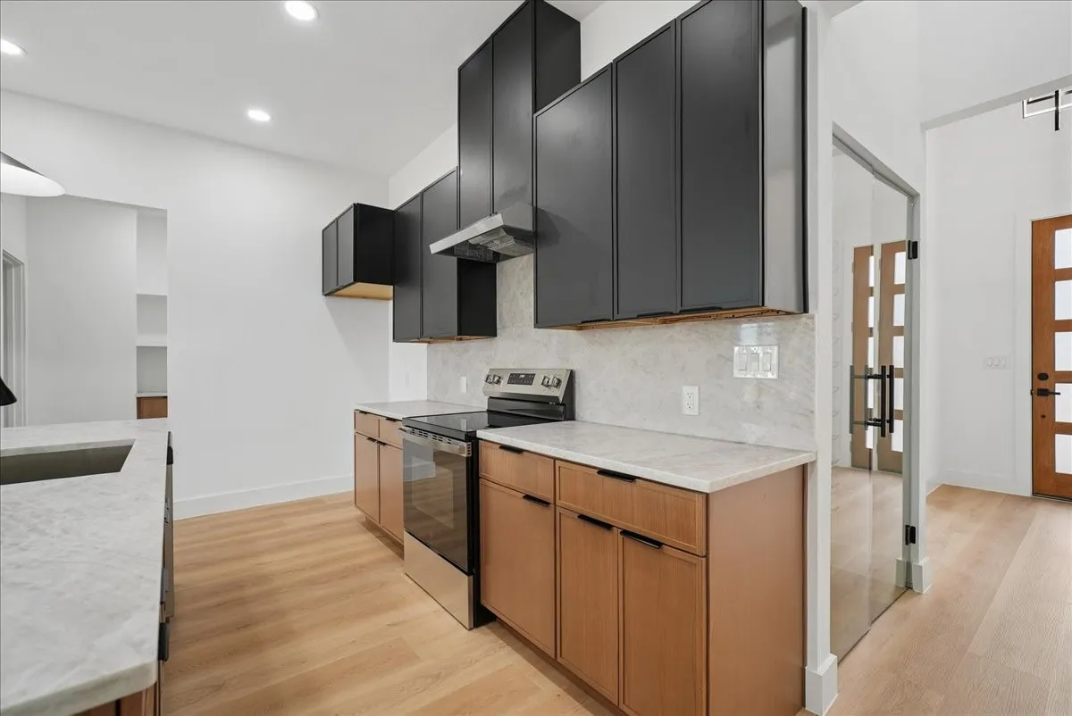 Modern kitchen featuring two-tone cabinetry, stainless steel range, light-toned wood-finish flooring, and recessed lighting