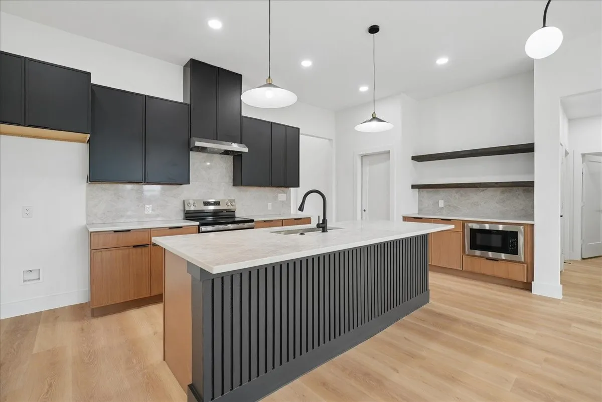 Kitchen featuring wood-finish flooring, a central island with a light-toned countertop, a range with an overhead vent, and a built-in microwave