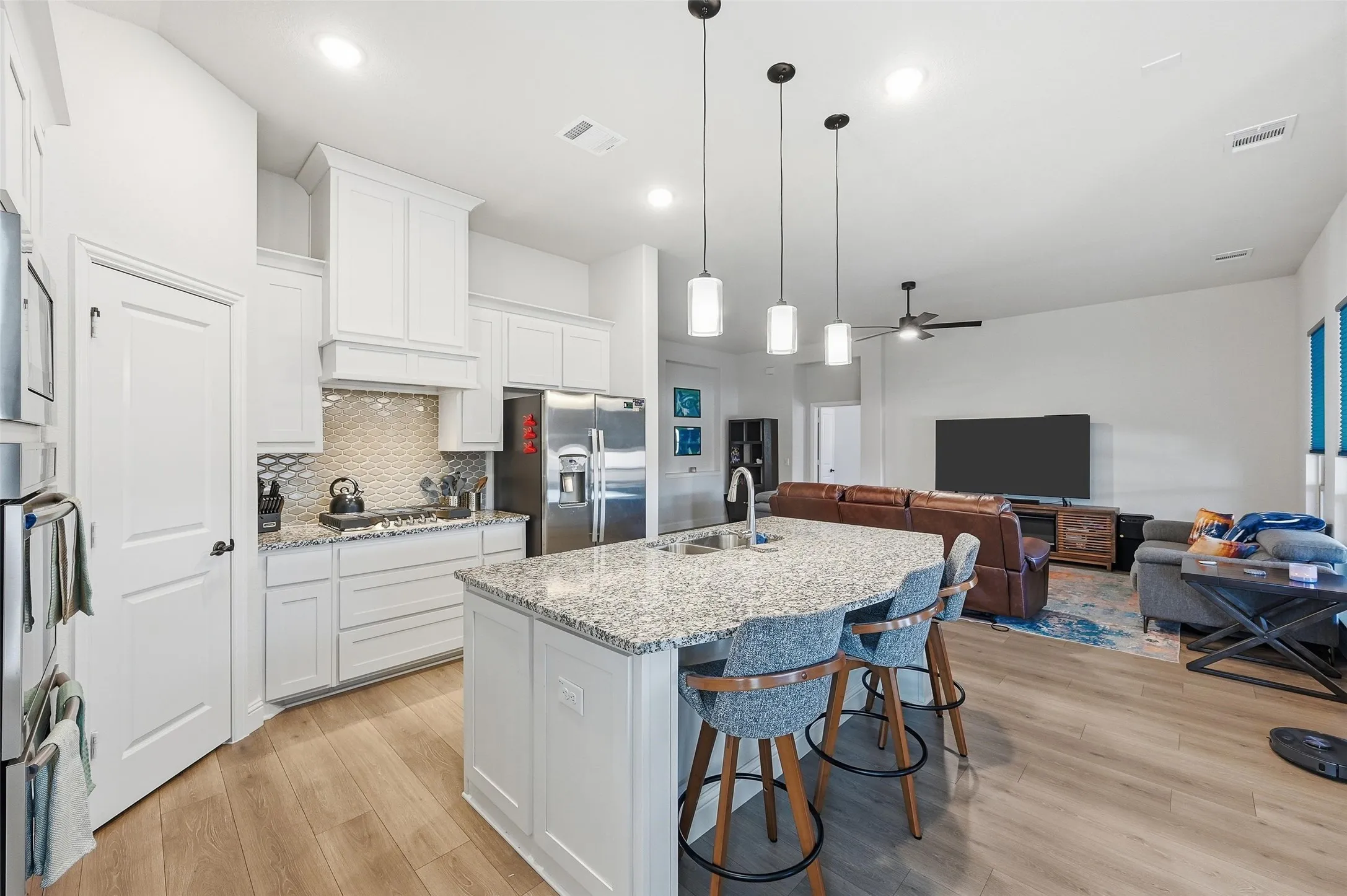 Kitchen island featuring a granite-style countertop, undermount sink, and three pendant lights