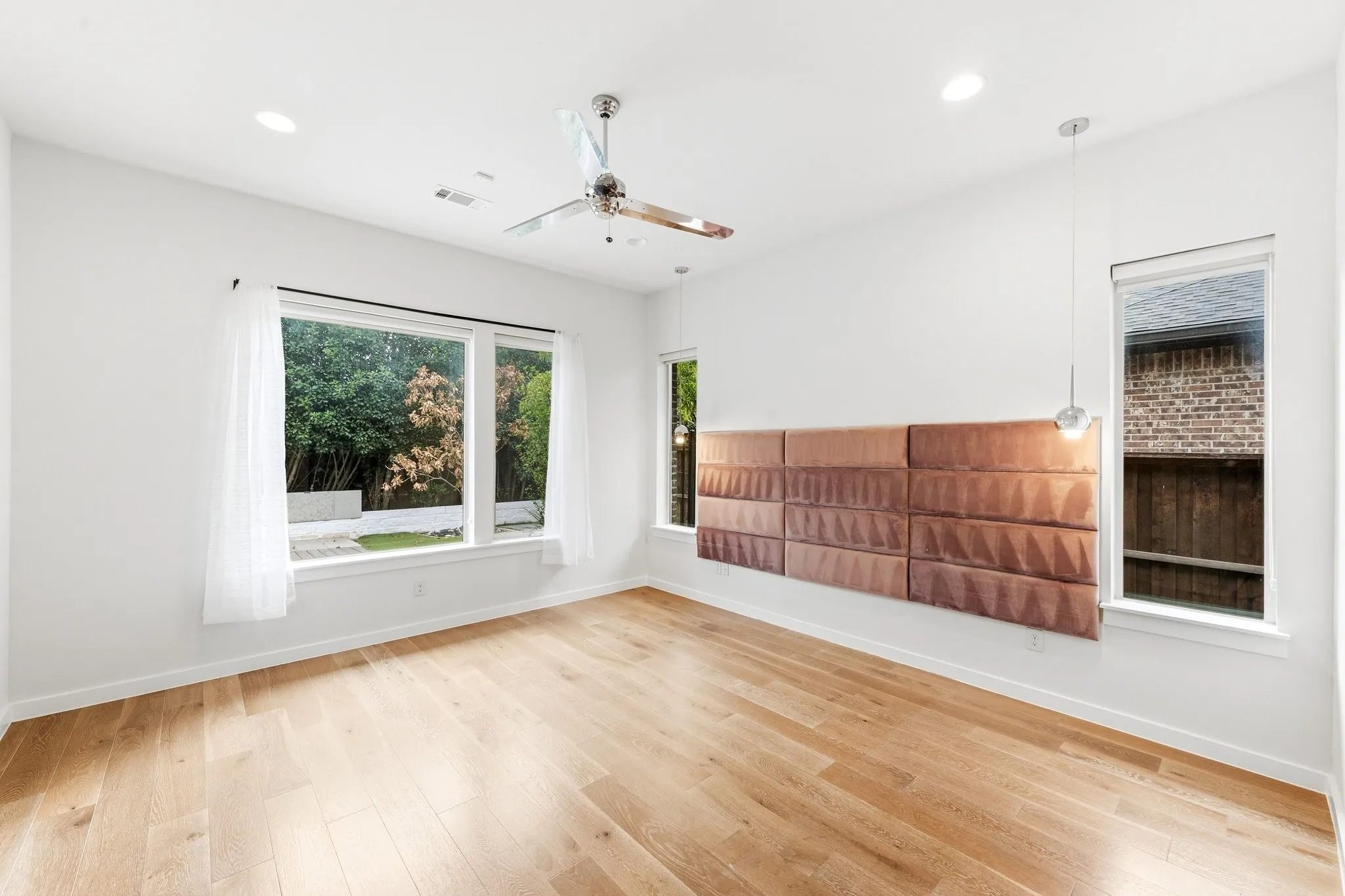 Sun-drenched primary bedroom featuring high ceilings, warm hardwoods, and scenic backyard vistas.