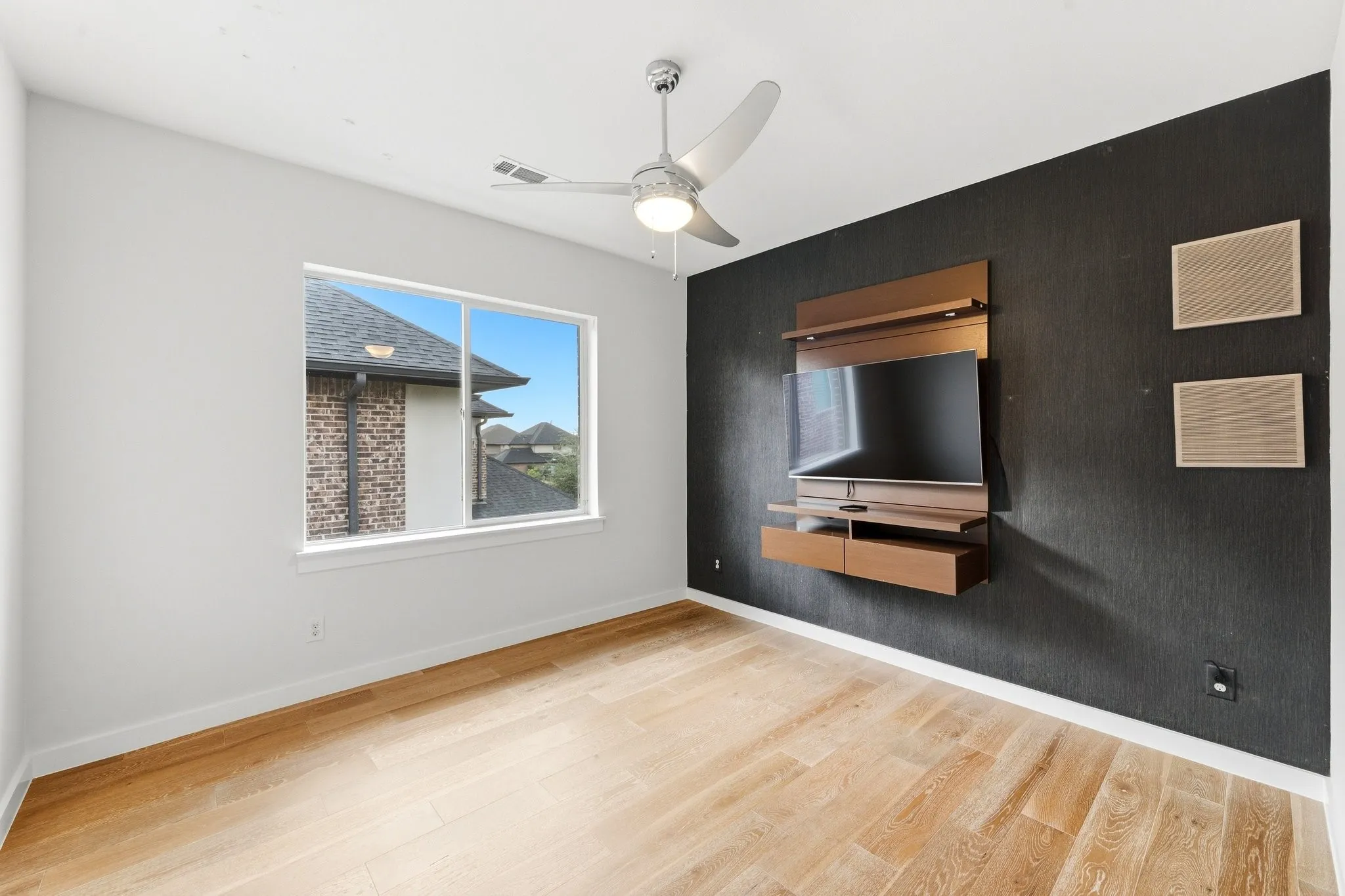 upstairs secondary bedroom featuring rich flooring, ceiling fan, TV, and large bright window.
