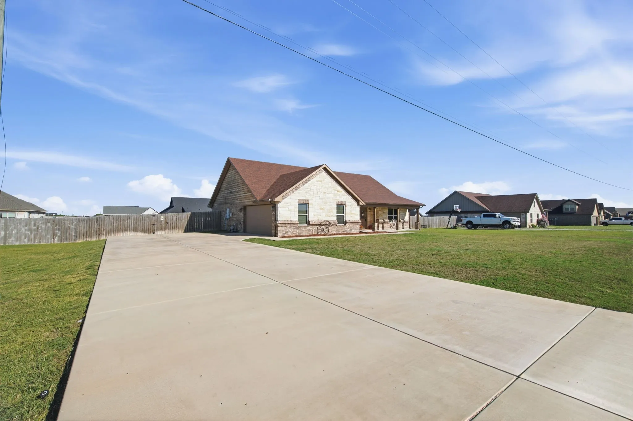 Brick and stone exterior with a covered porch, an attached garage, a concrete driveway, and a fenced yard