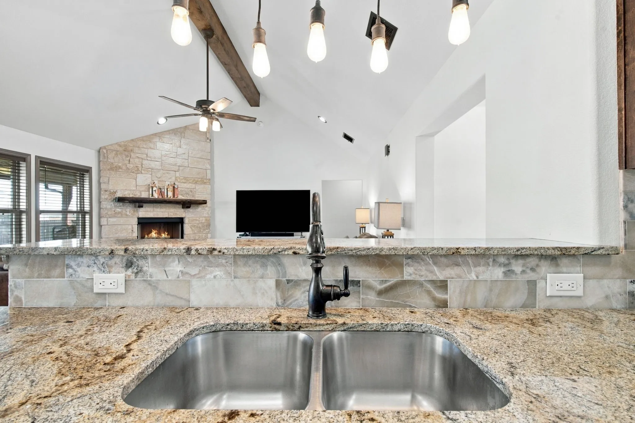 Double basin stainless steel sink with a dark-finish faucet, granite countertops, and a tile backsplash