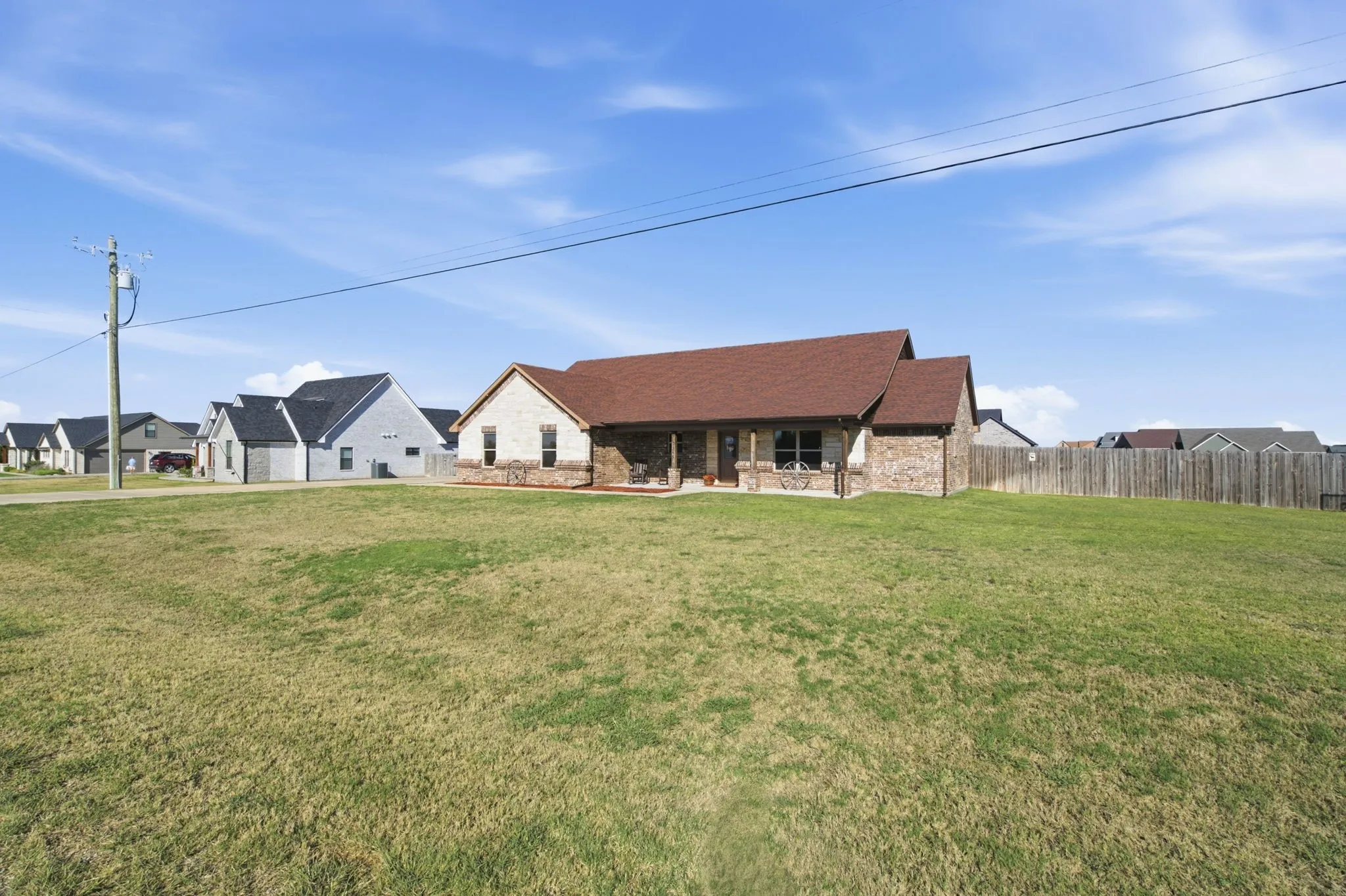 Single-story home featuring a brick and stone exterior, a covered front porch with columns, a prominent front lawn, and a fenced backyard