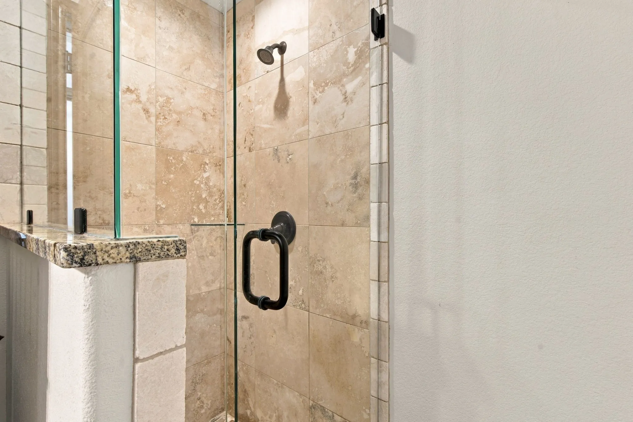 Glass-enclosed shower with a bronze showerhead, bronze handle, and stone tile surround