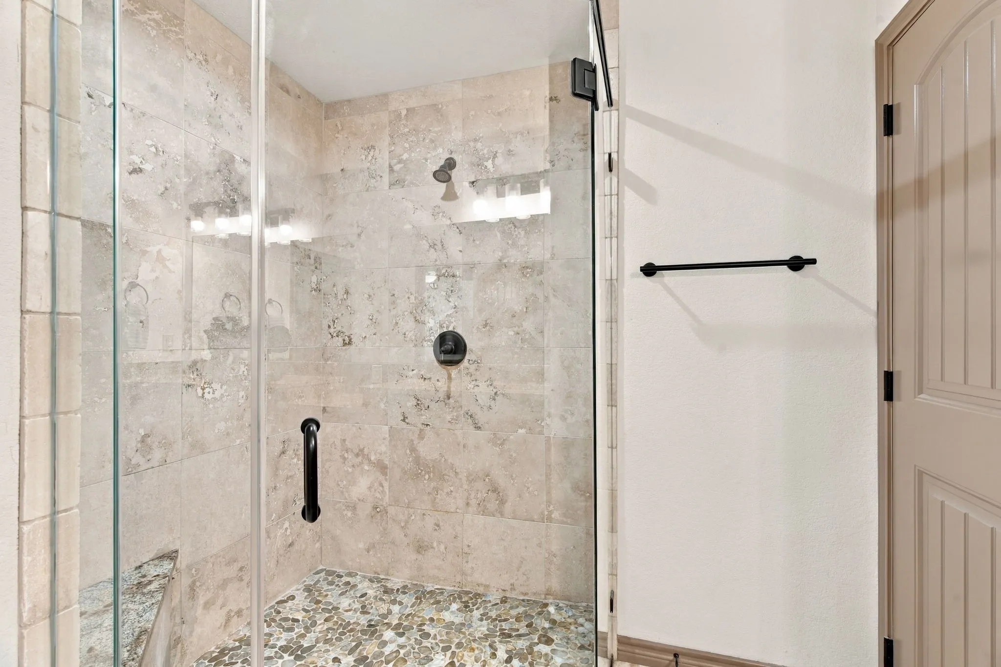 Glass-enclosed shower featuring natural stone tile walls and a pebble floor