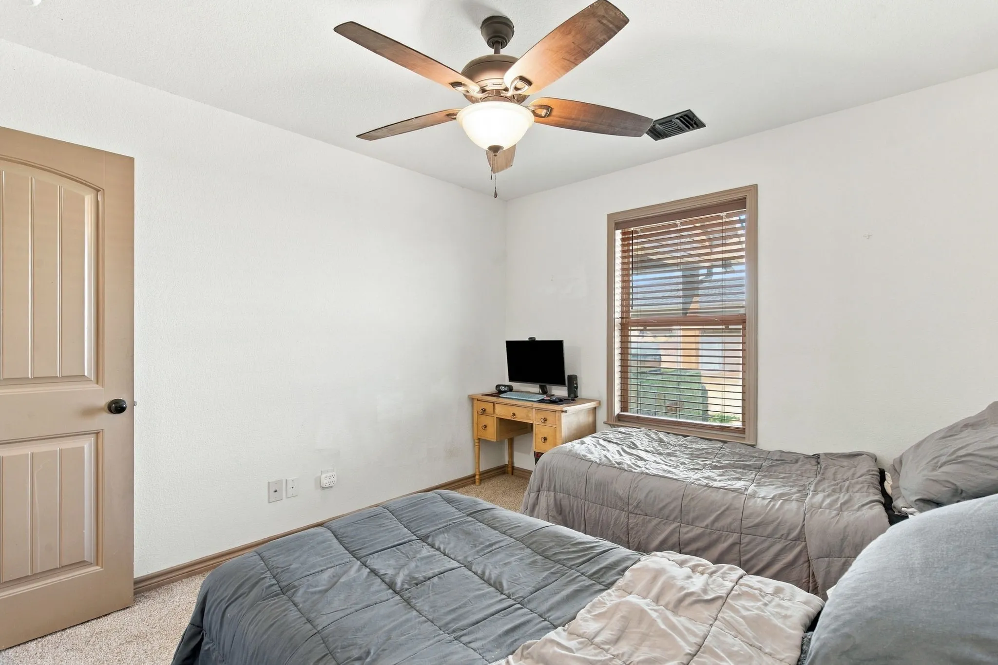 Carpeted flooring, a ceiling fan with light fixture, a window with blinds, and a paneled door with a round black knob