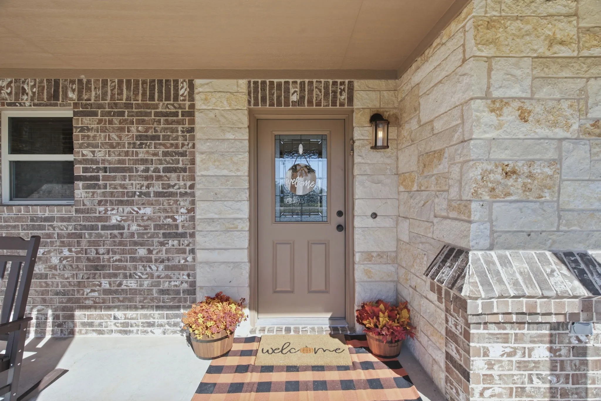 Exterior featuring a brick and stone facade, covered entry, and a glass-paneled front door with an exterior light fixture