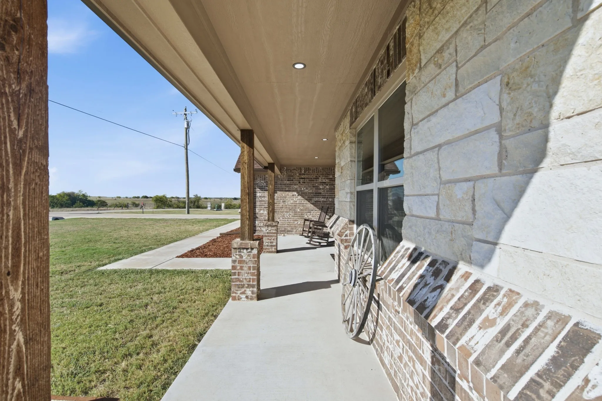 Covered porch with exposed wood columns, brick accents, and stone facade