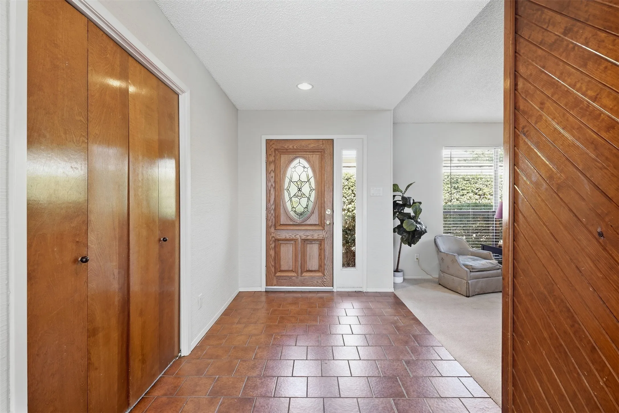 Wood-paneled entry door with decorative glass insert, recessed lighting, and tile flooring