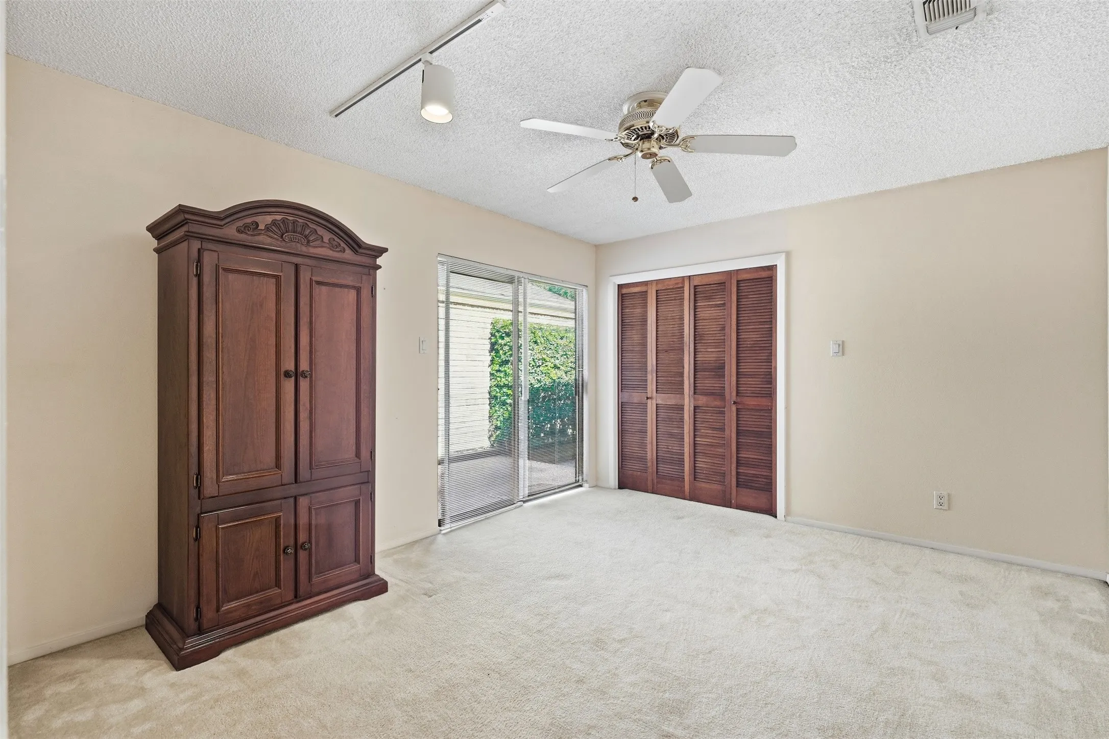 Sliding glass doors, track lighting, ceiling fan, and louvered bifold closet doors