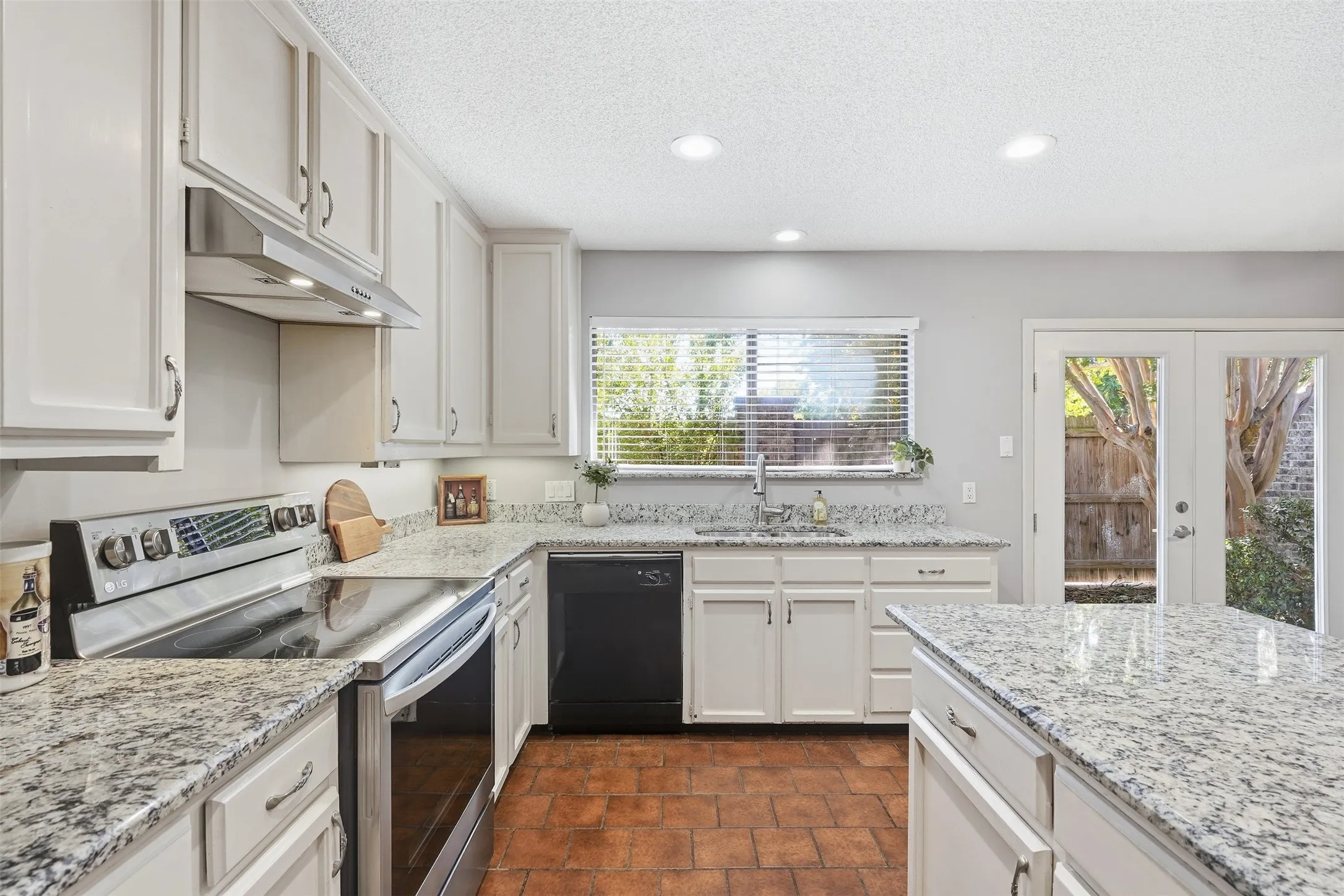 White cabinetry, granite countertops, tile flooring, recessed lighting, and a stainless steel range hood