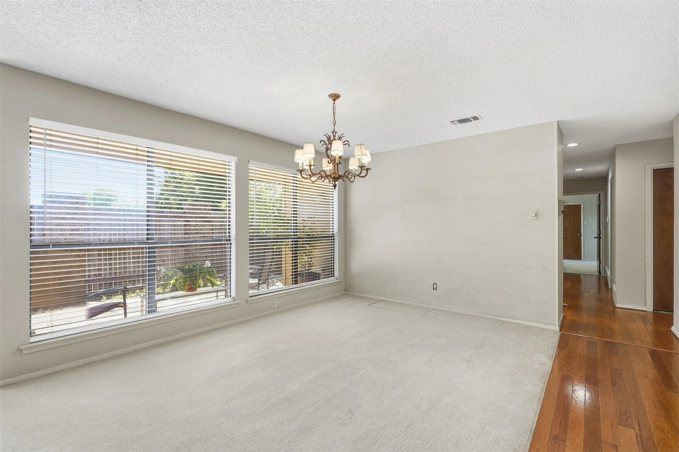 Bright room featuring multiple windows with horizontal blinds, a decorative chandelier, and a combination of carpet and wood-finish flooring