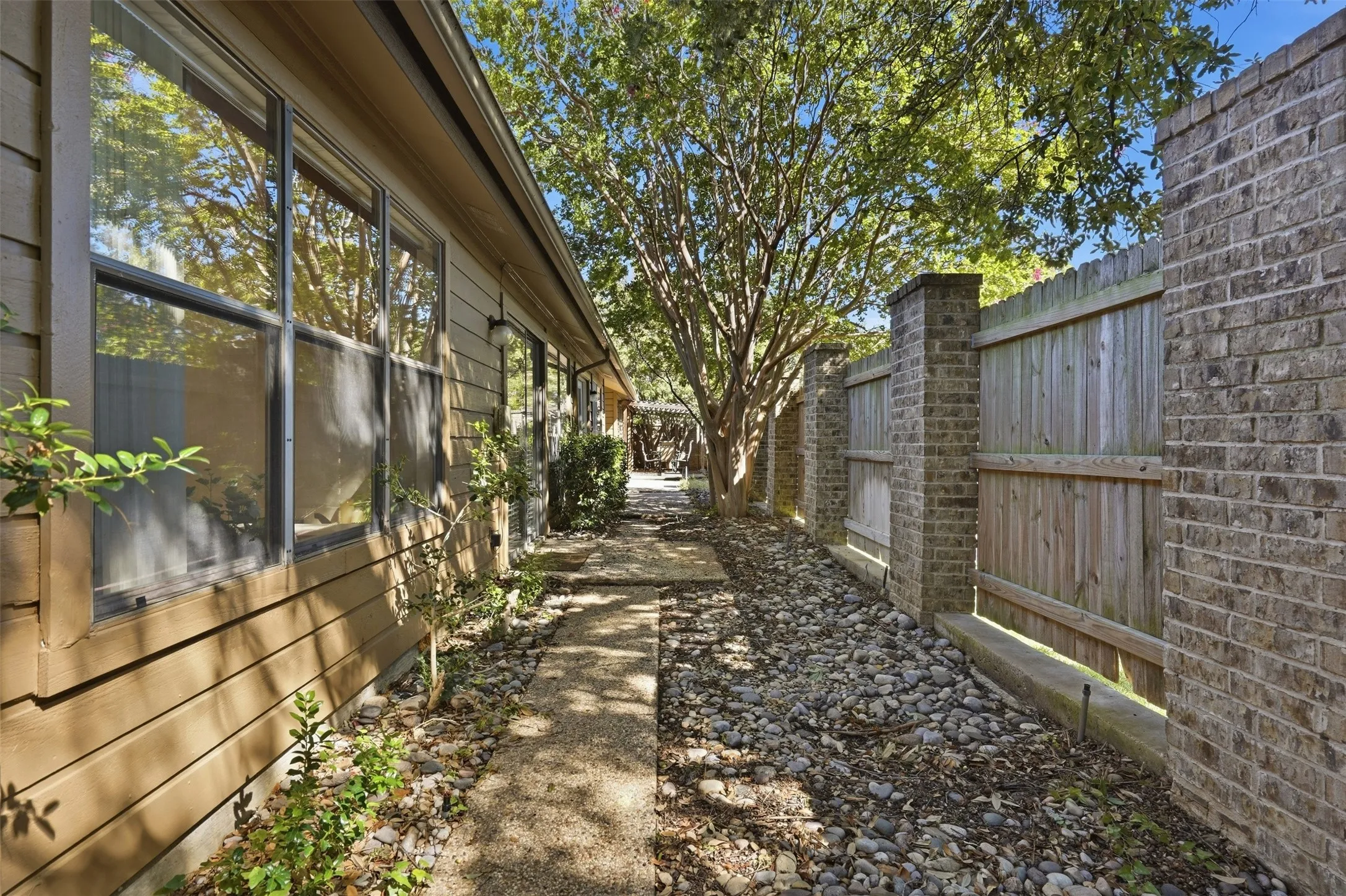 Stone pathway with surrounding river rock, wood siding exterior, multi-pane windows, and a brick and wood fence