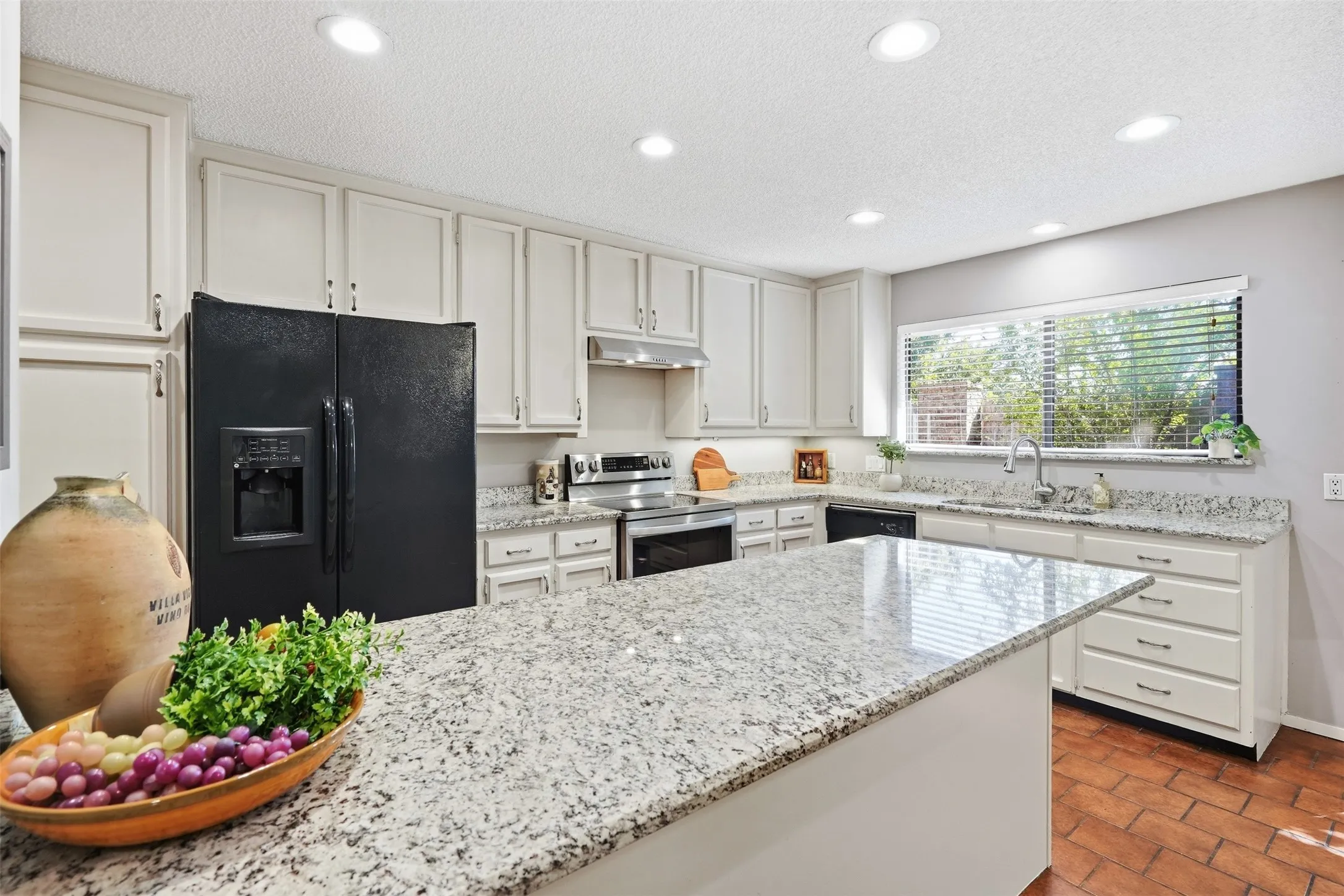 Kitchen featuring an island with stone-finish countertop, white cabinetry, recessed lighting, and a window with blinds
